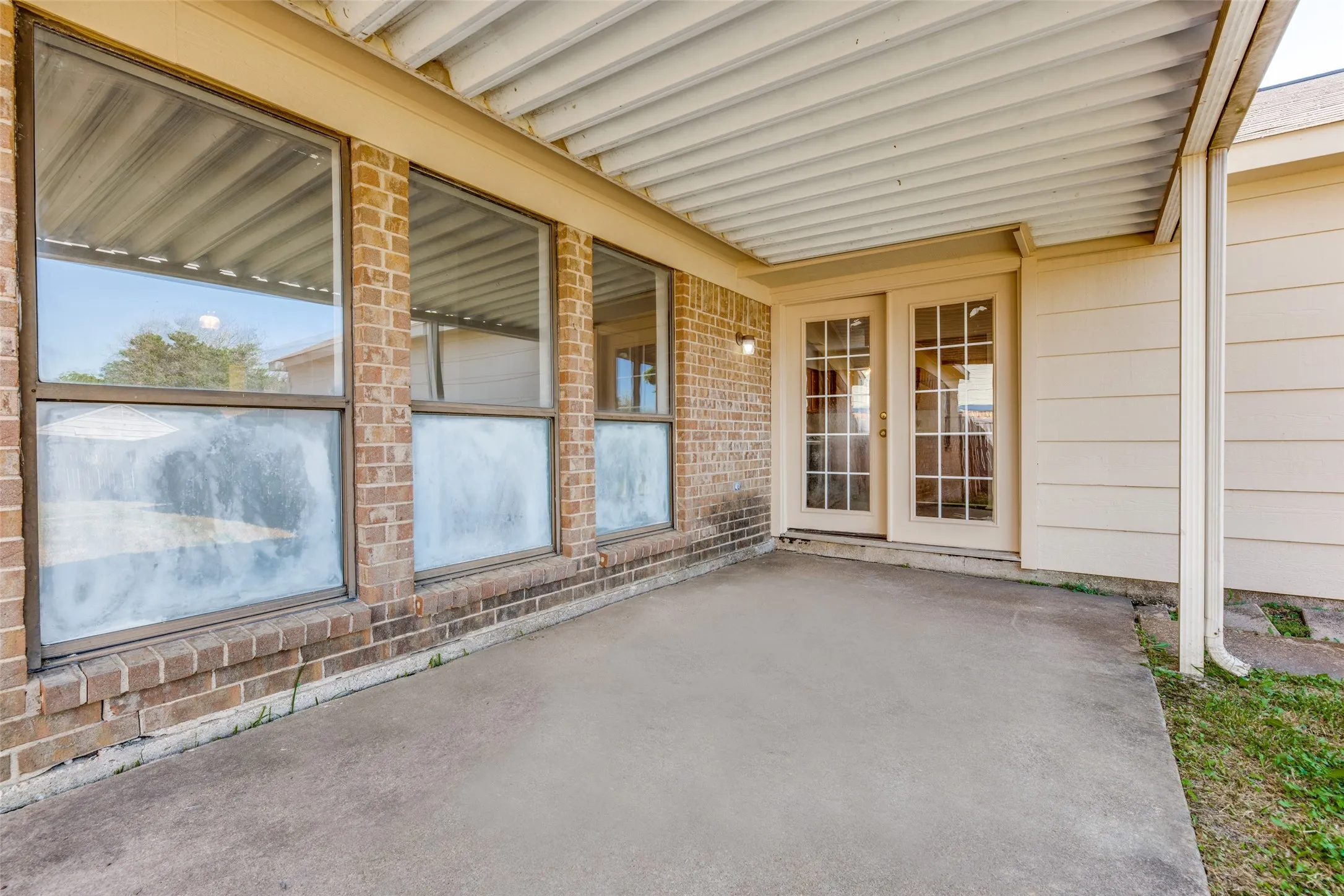 Covered concrete patio with a brick exterior wall and multiple windows