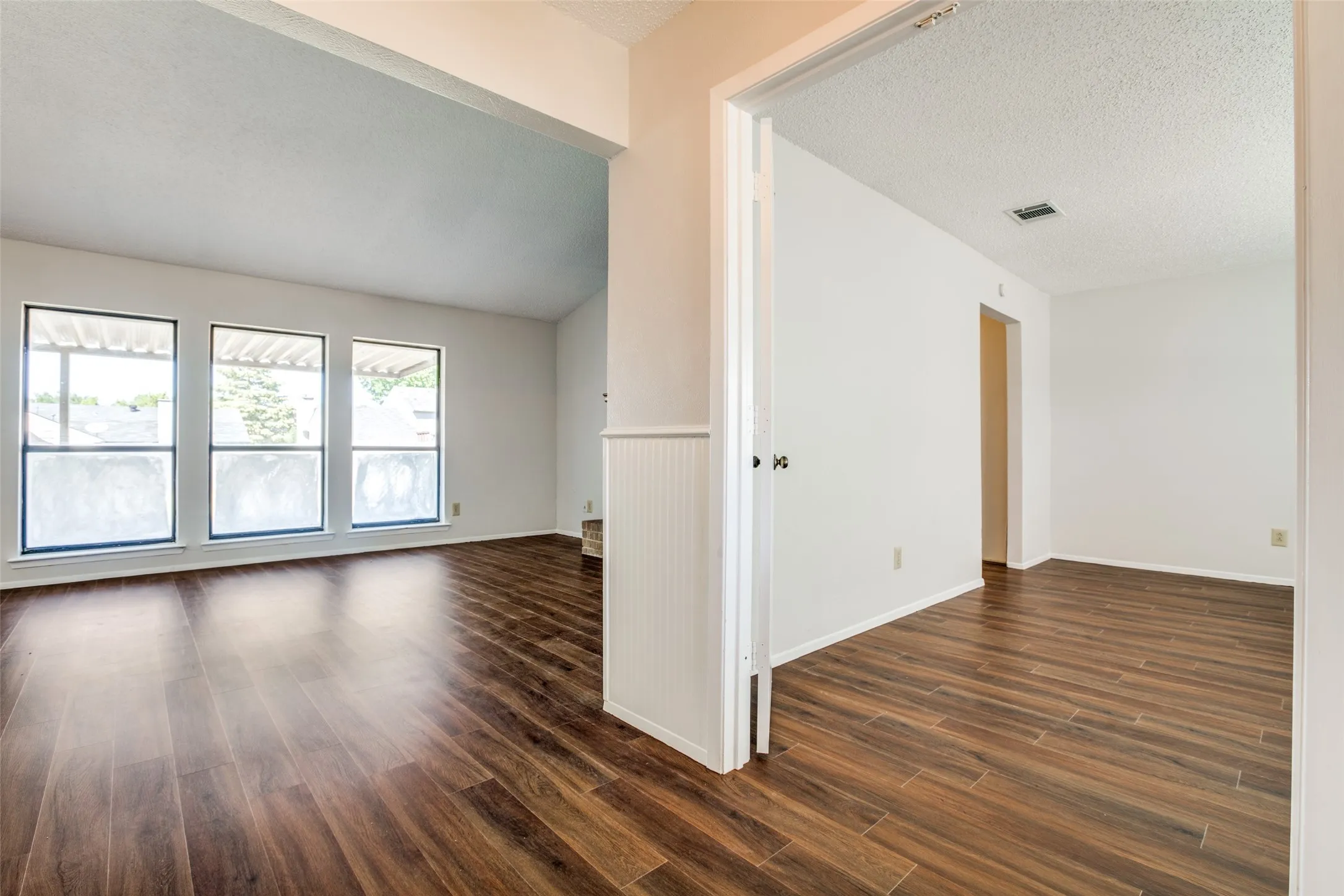 Bright, open living spaces showcase rich wood-finish flooring throughout, complemented by large multi-pane windows flooding the rooms with natural light