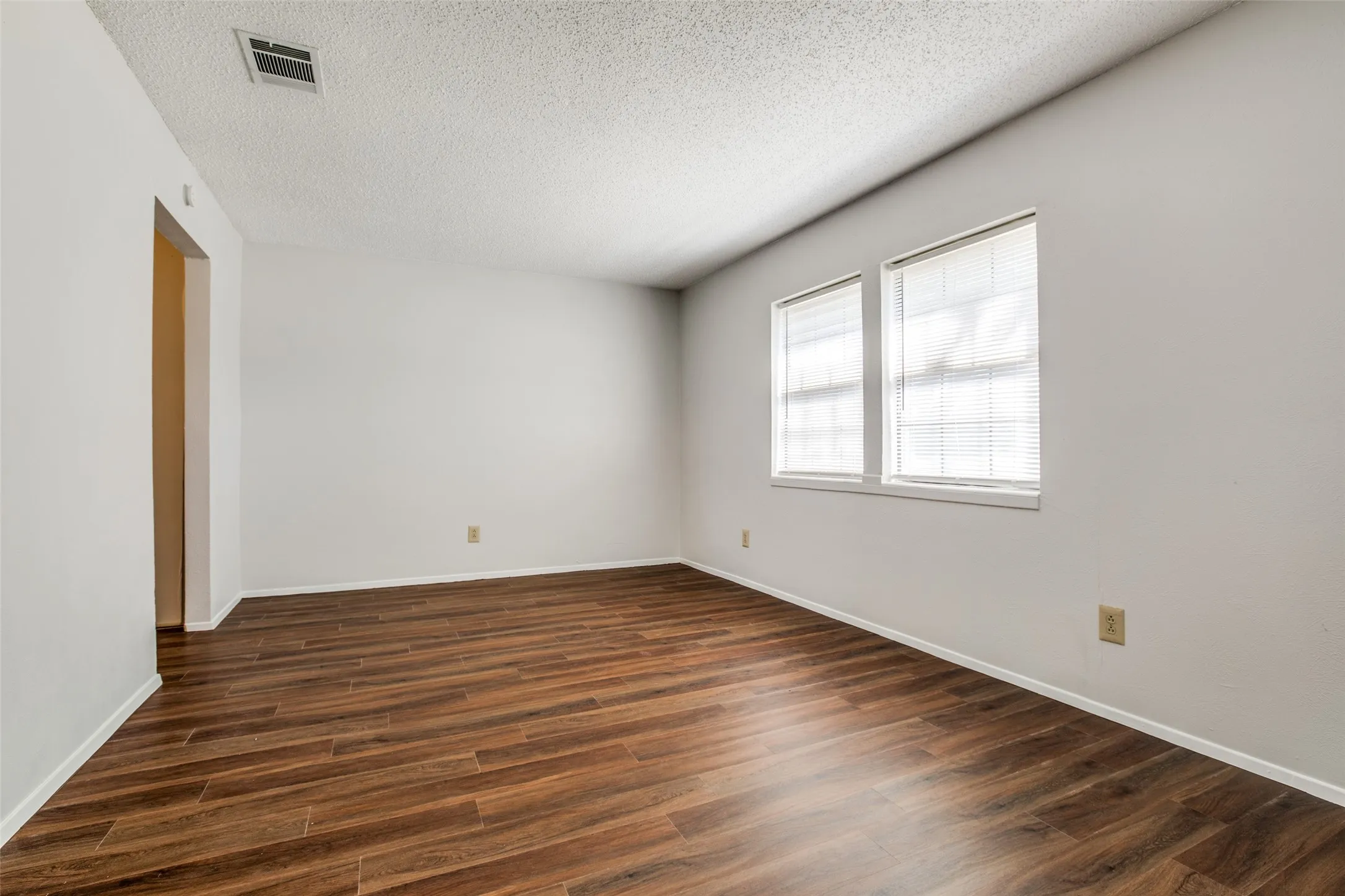 Wood-finish flooring throughout, bright white walls, and two windows with blinds
