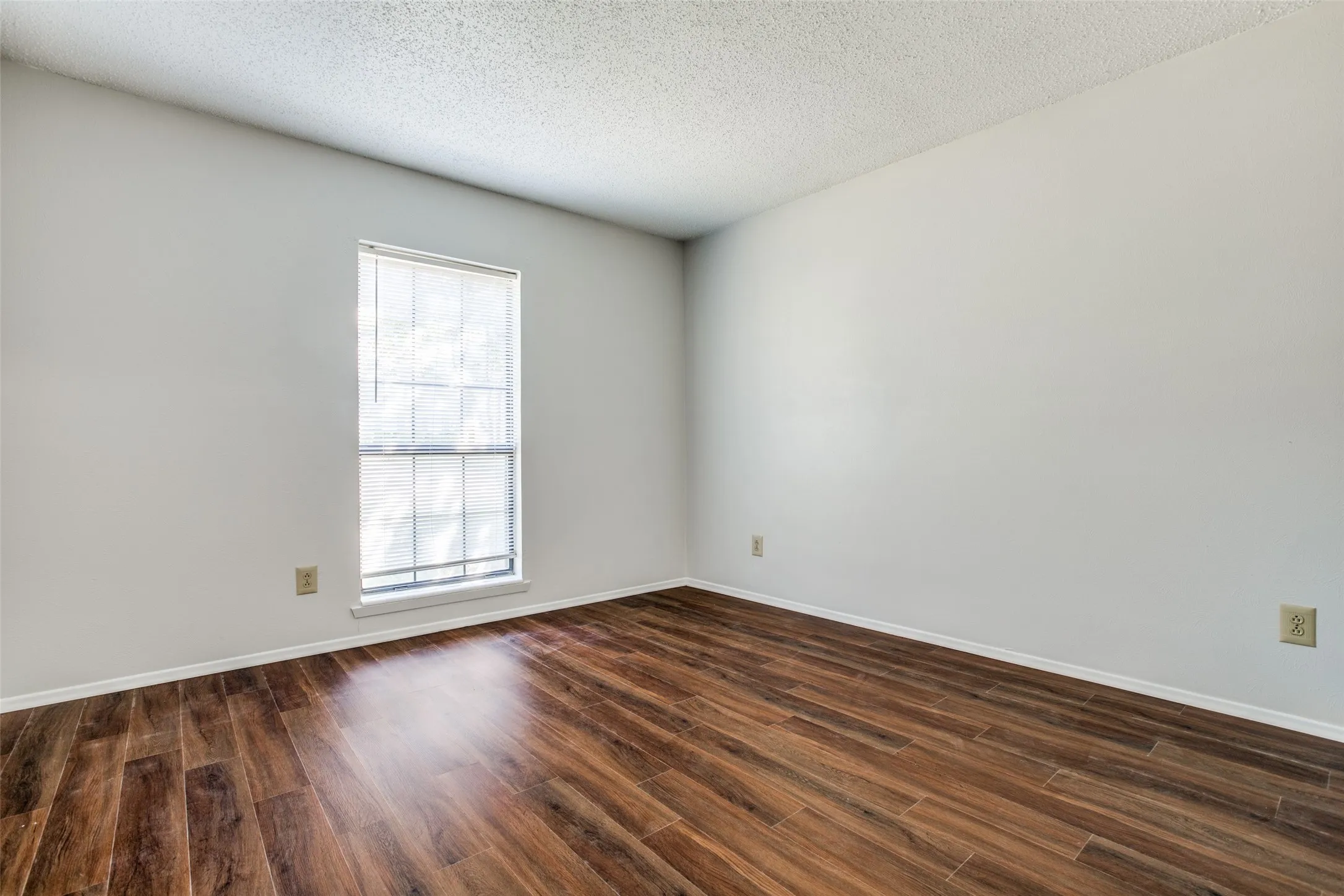 Warm wood-finish flooring complemented by light-toned walls and a window with blinds