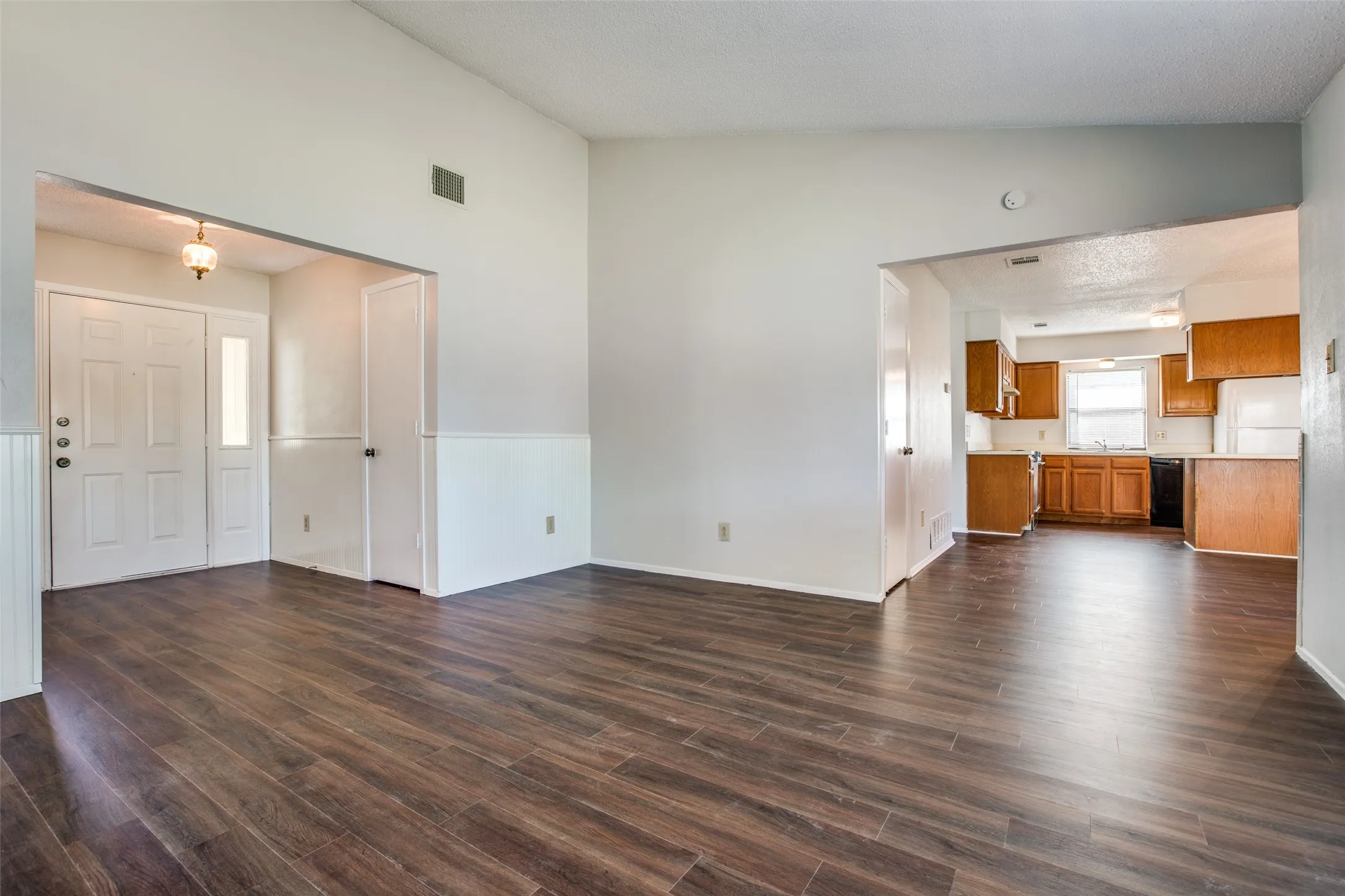 Wood-finish flooring throughout, with a front entry featuring a transom window, and a kitchen with wood cabinetry and a window above the sink