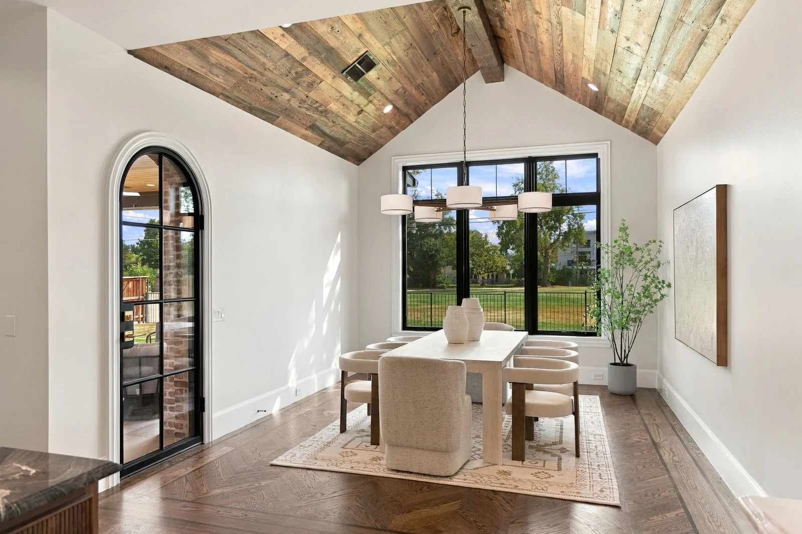 Vaulted ceiling with wood-finish planks, large black-framed window, arched glass-panel door, and herringbone wood-finish flooring