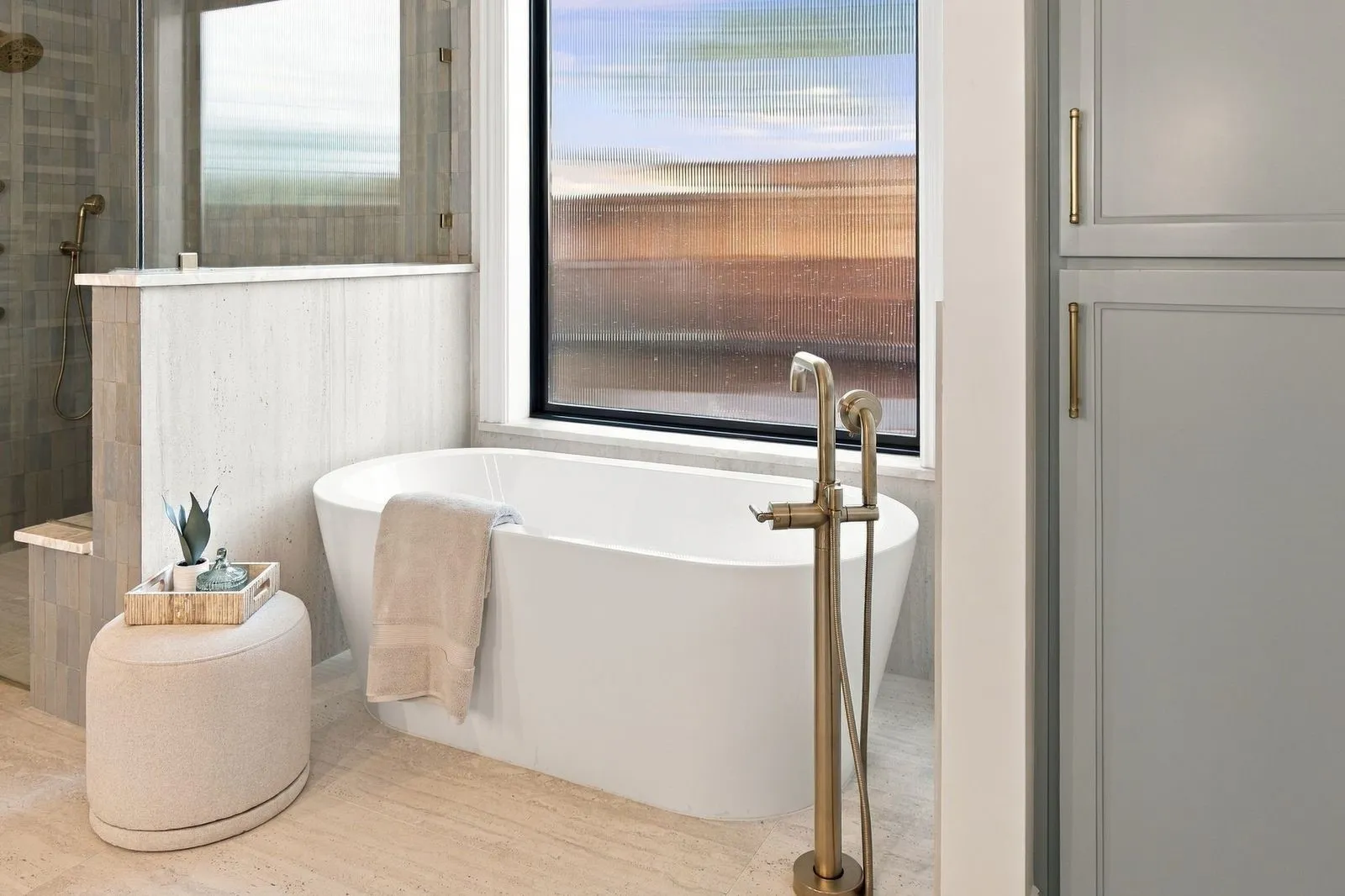 Freestanding soaking tub with a floor-mounted brass faucet, tile flooring, and integrated shower with glass enclosure