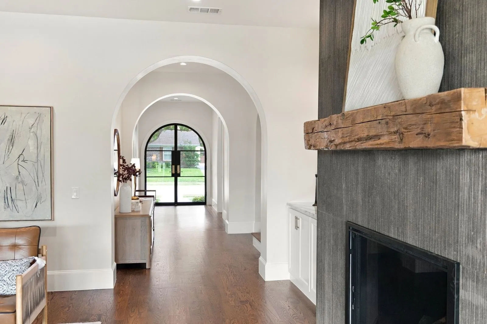 Arched entryways, dark wood-finish flooring, a fireplace with a rough-hewn wooden mantel, and a built-in cabinet