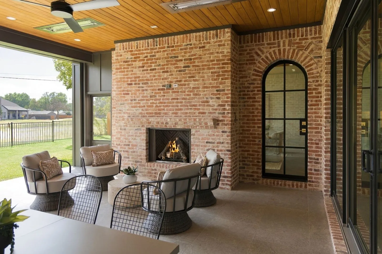 Covered patio featuring a brick fireplace, wood-plank ceiling, and a black wrought iron arched door