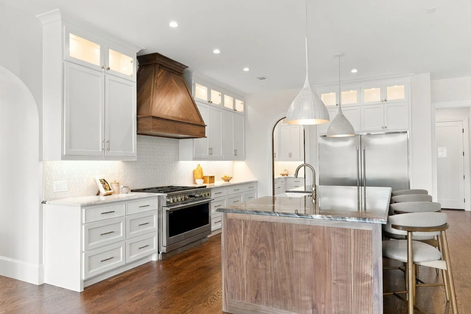 Gourmet kitchen featuring a wood-panel range hood, stainless steel appliances, white shaker cabinetry, and a large center island with a wood-finish base and stone countertop