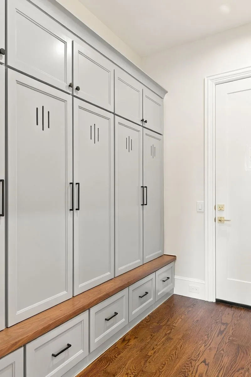 Built-in cabinetry with light gray shaker-style doors, black hardware, an integrated wood-finish bench, and wood-finish flooring