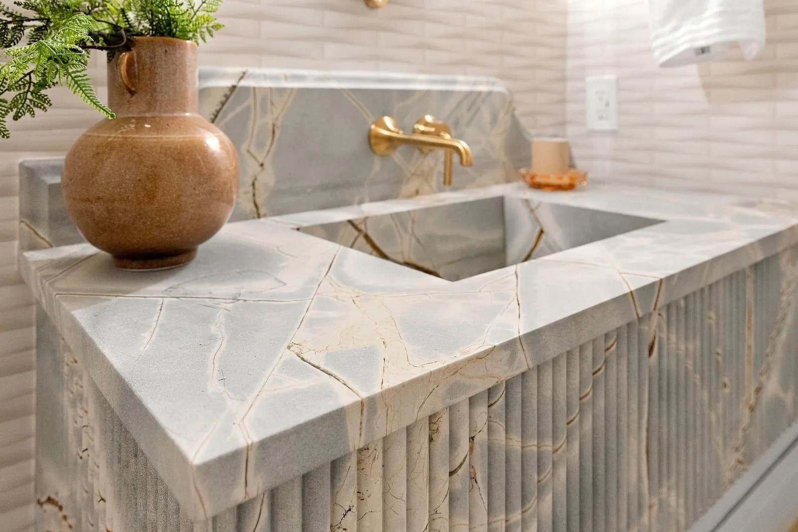 Integrated sink with a fluted vanity base, veined stone countertop, and brass wall-mounted faucet