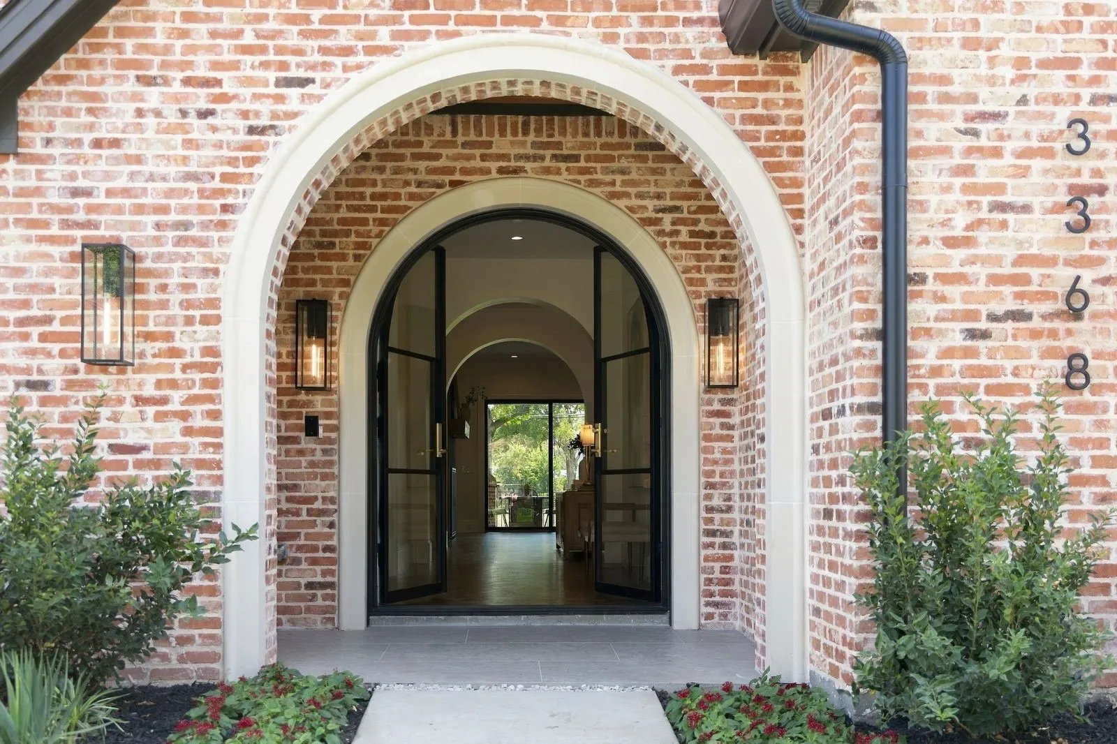 Red brick exterior with a white arched entry, featuring black-framed glass double doors and two exterior wall sconces