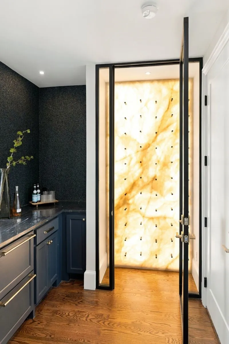 Hardwood flooring, dark blue cabinetry with gold-tone hardware, dark countertop, textured dark wall covering, and a backlit translucent panel