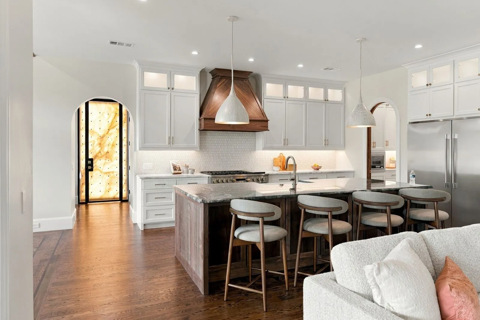 Gourmet kitchen with wood-finish flooring, white cabinetry, a wood range hood, a kitchen island with a stone countertop, and stainless steel appliances