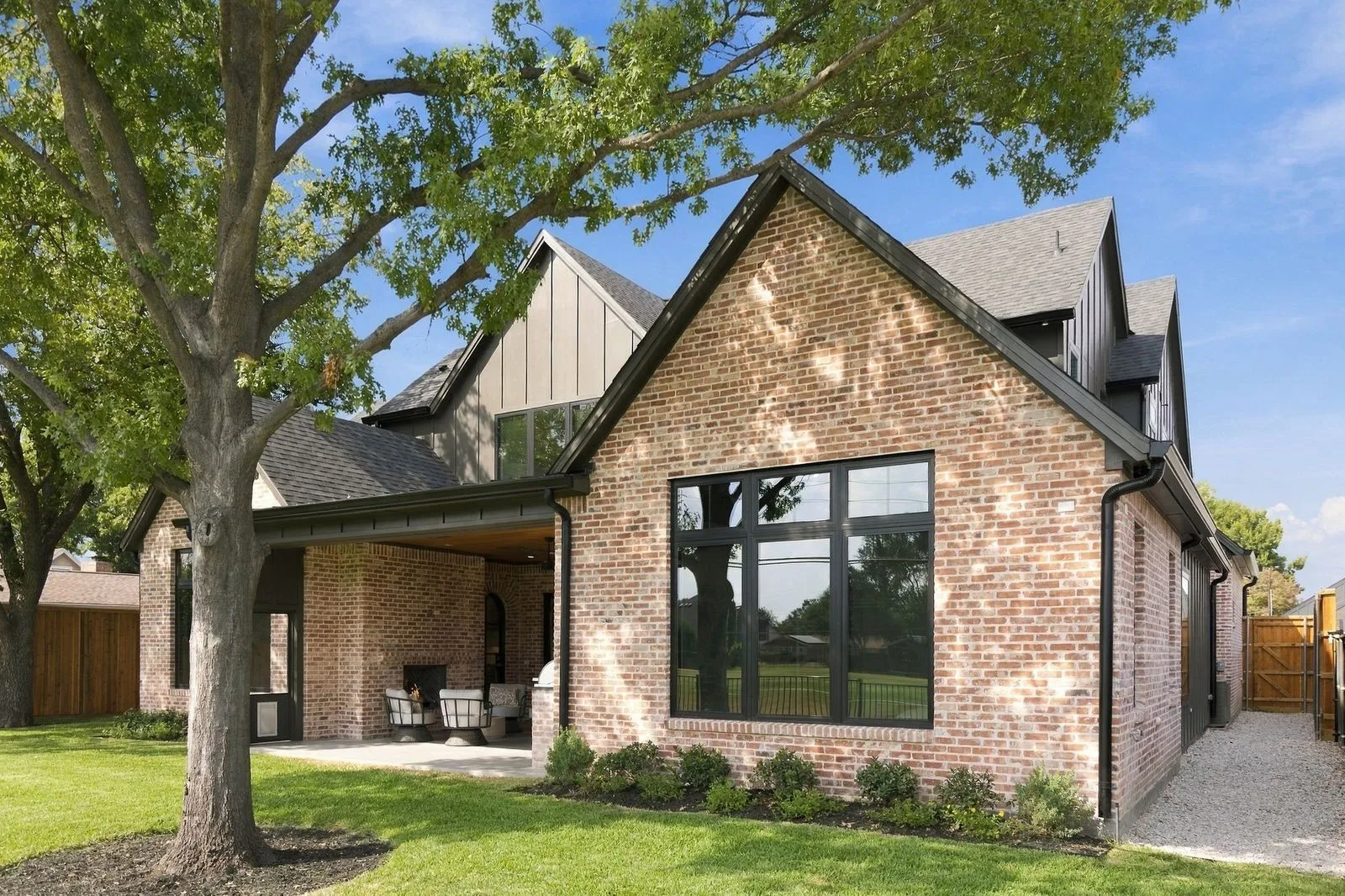 Brick exterior with black-framed windows, a covered patio, and a gravel walkway