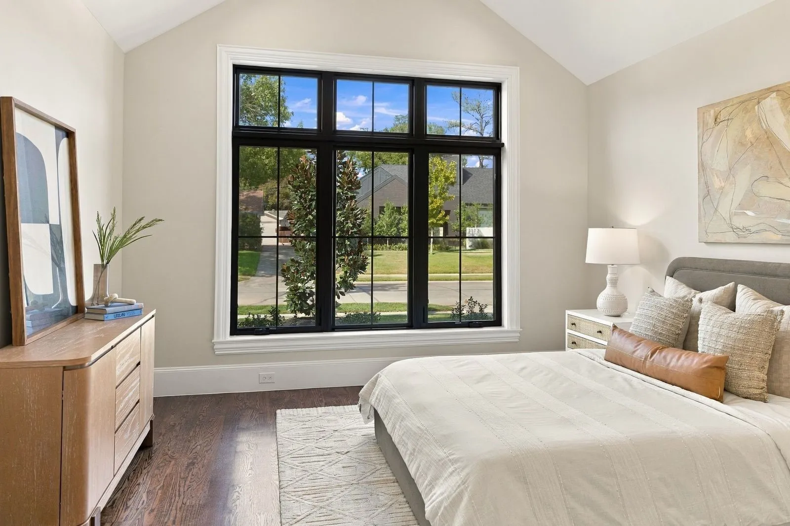 Vaulted ceiling, large multi-pane window with dark trim, hardwood flooring, and light-toned walls