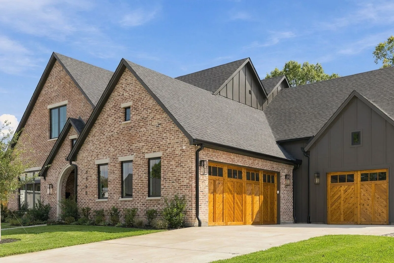 Brick and vertical siding exterior with gabled roofs, multiple wooden garage doors, and a concrete driveway