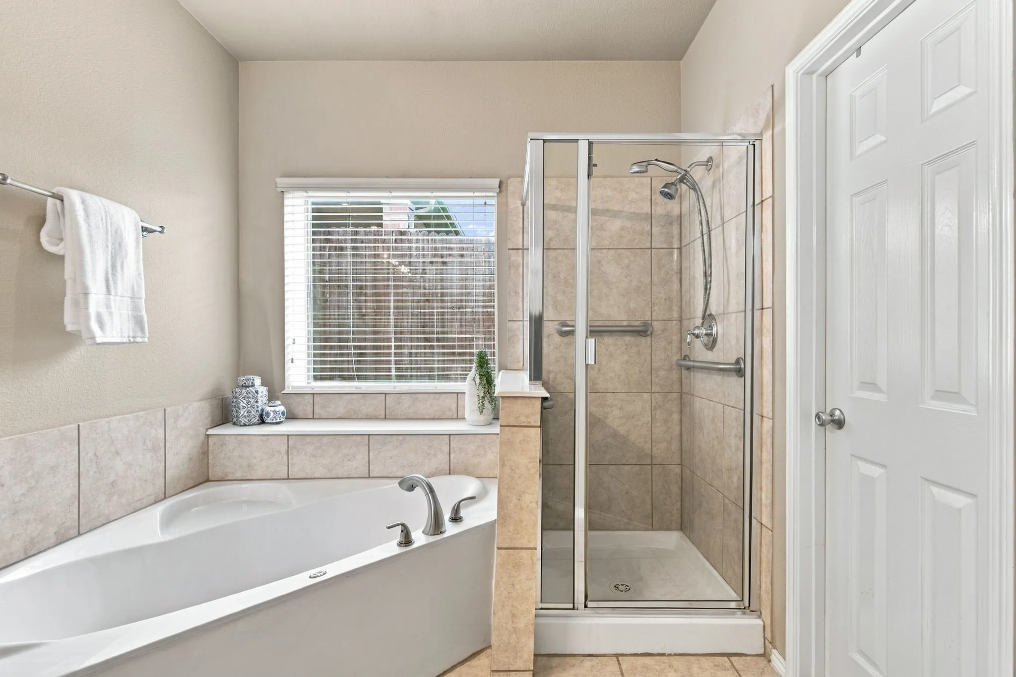 Corner soaking tub, tiled shower with glass enclosure, chrome fixtures, and a privacy window with blinds