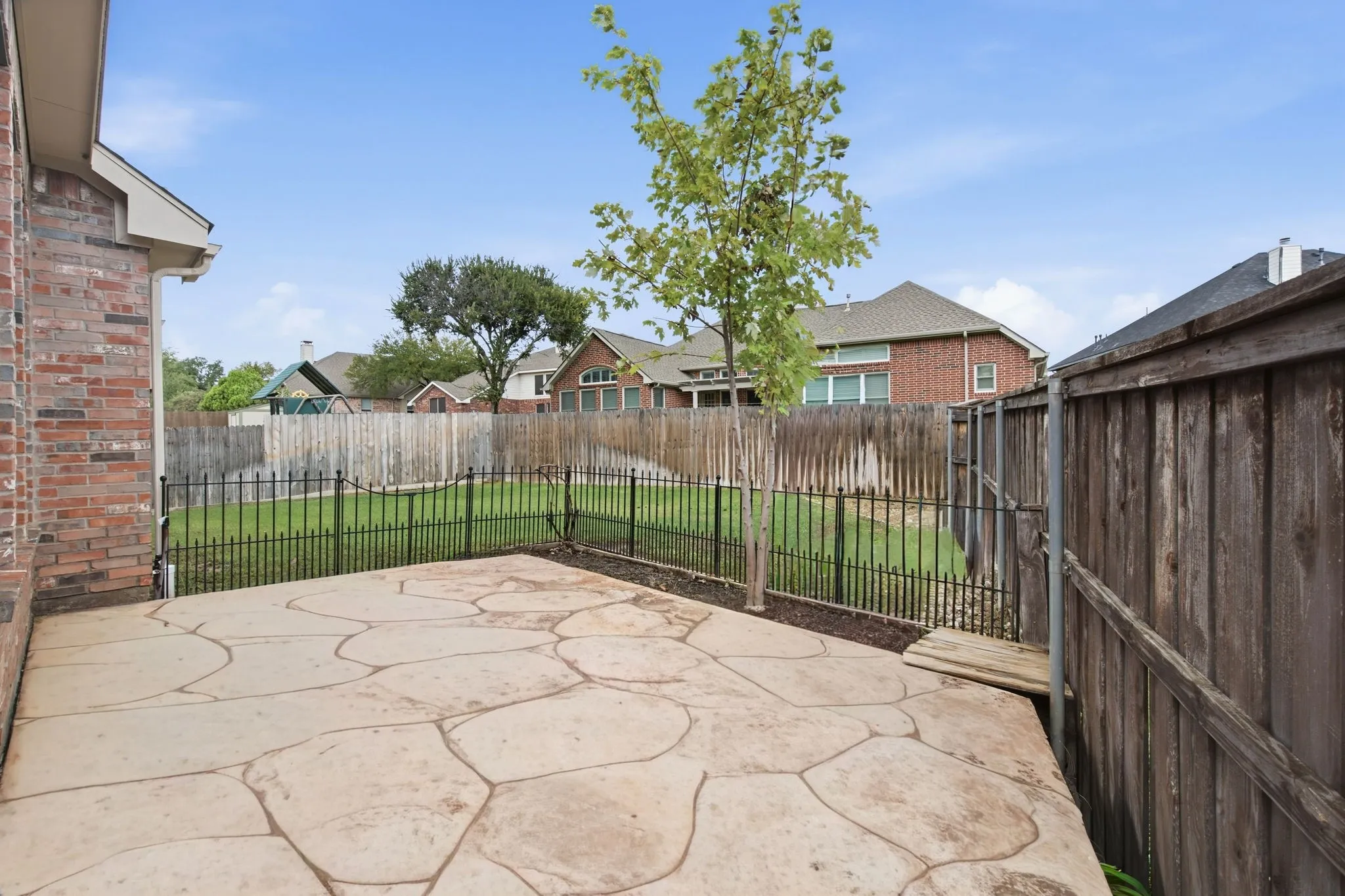 Expansive stamped concrete patio with direct access to a fenced backyard featuring a manicured lawn and mature landscaping