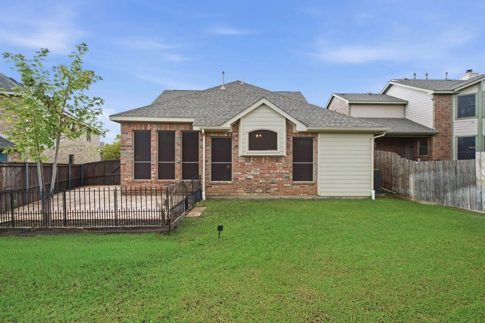 The metal black fencing can be removed easily. Expansive rear lawn, brick exterior with siding accents, fenced patio area, and architectural shingle roofing