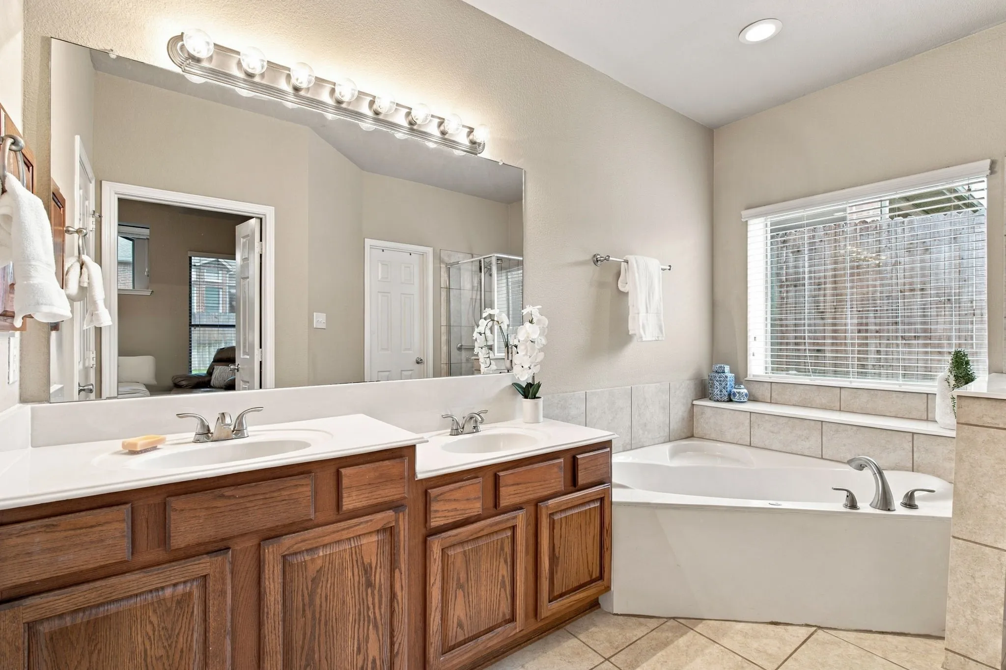 Dual vanity with integrated sinks, wood-finish cabinetry, built-in soaking tub, tile surround, and tile flooring