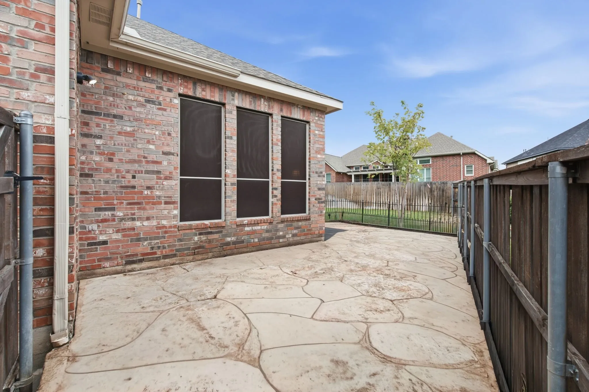 Stained concrete patio with a brick exterior, three windows with solar screens, and a wood privacy fence
