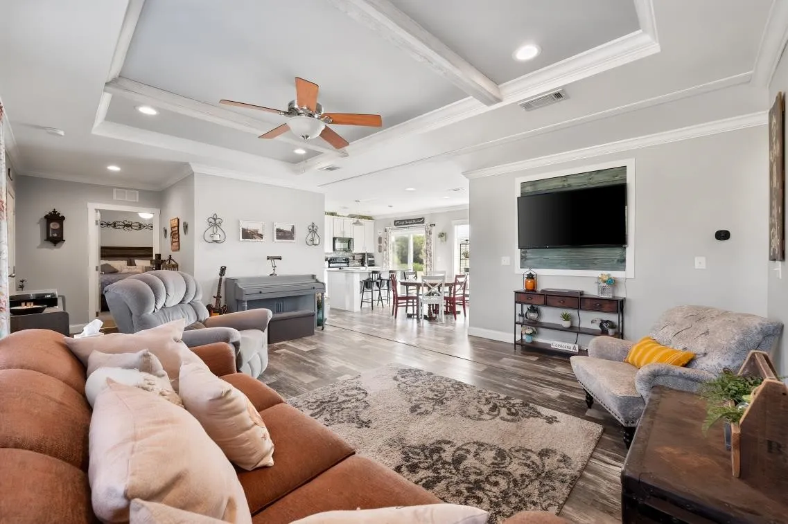 Tray ceiling with exposed beams, wood-finish flooring, recessed lighting, ceiling fan, and built-in wall niche with wood paneling