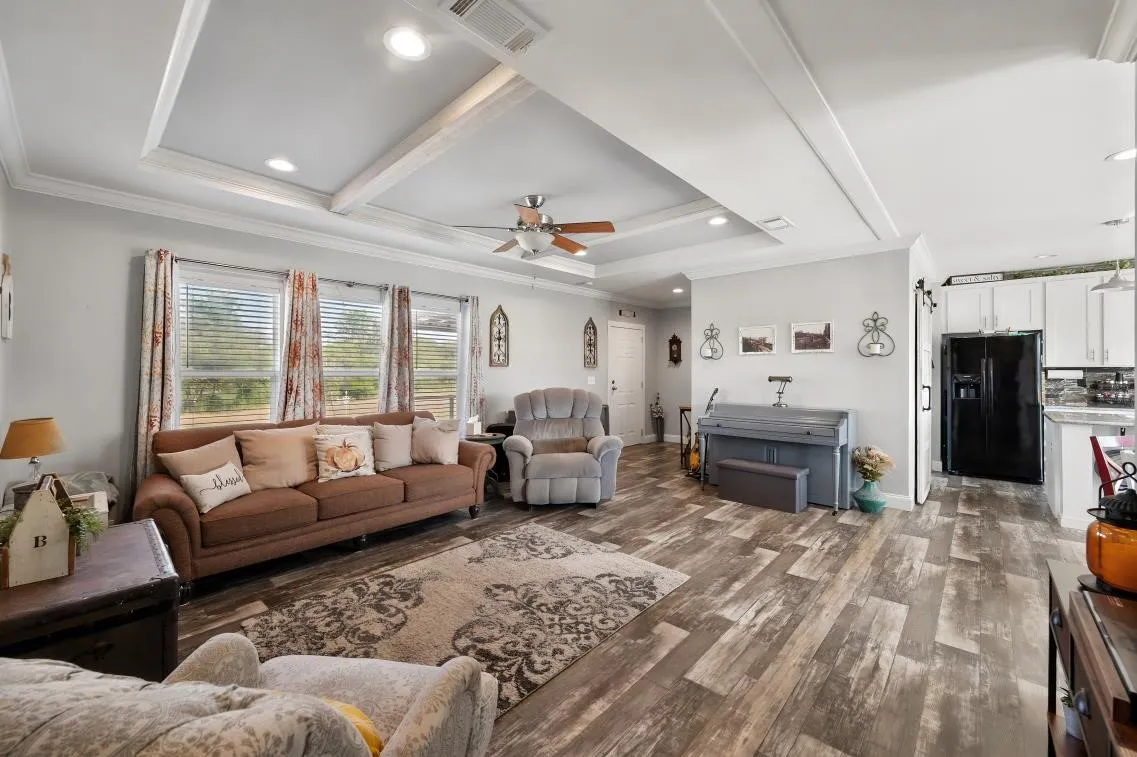 Open concept living room showcasing a tray ceiling with recessed lighting and a ceiling fan, wood-finish flooring, white cabinetry, and a black refrigerator