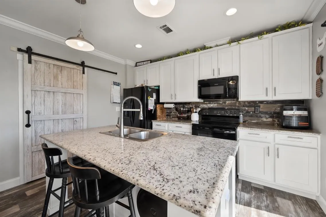 Kitchen featuring an island with a built-in sink, white cabinetry, dark wood-finish flooring, a barn door, and recessed lighting