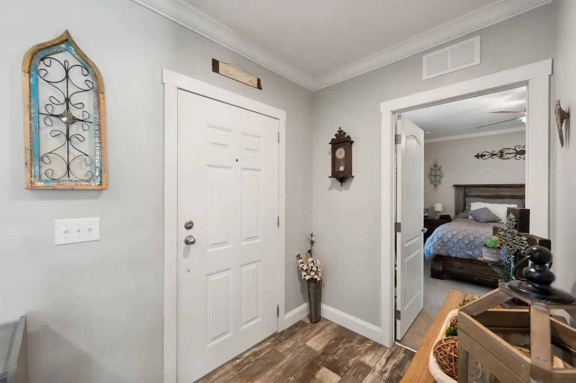 Wood-finish flooring with white trim, solid white paneled door, and crown molding