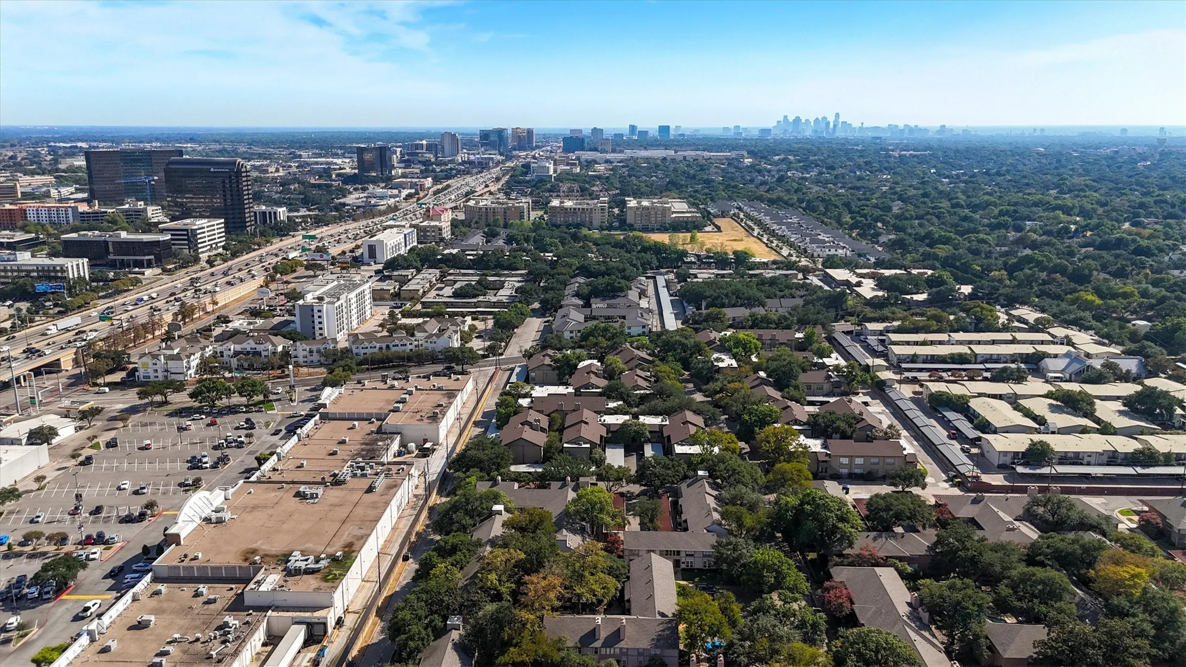Urban landscape featuring a distant skyline, extensive tree canopy, multi-lane highway system, and commercial structures
