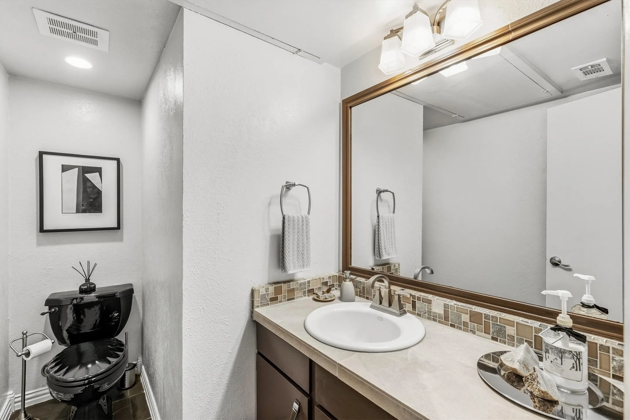 Vanity with integrated sink, mosaic tile backsplash, and large framed mirror