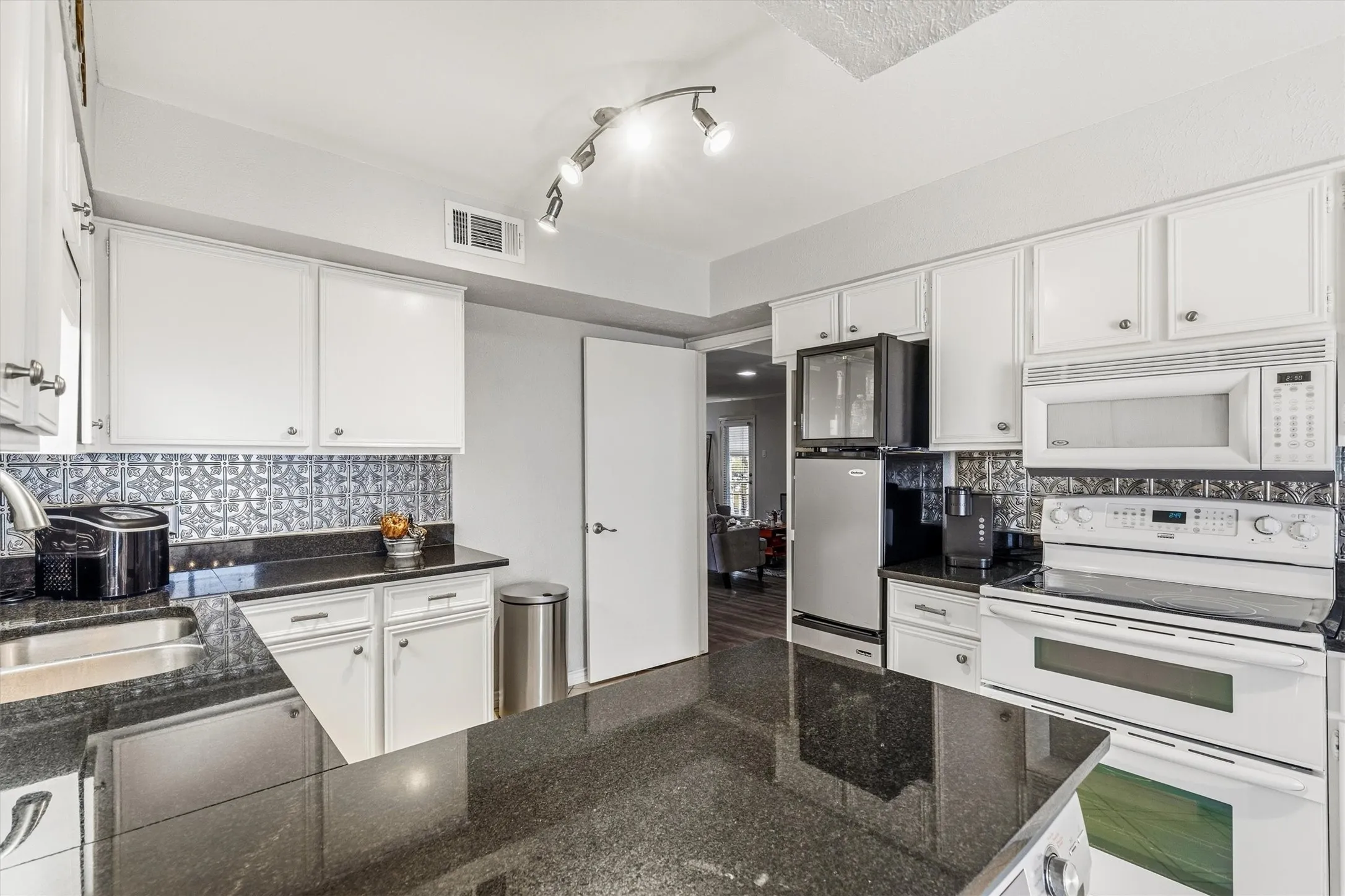 White cabinetry with brushed nickel hardware, black granite countertops, mosaic tile backsplash, stainless steel sink, and a range with a built-in microwave