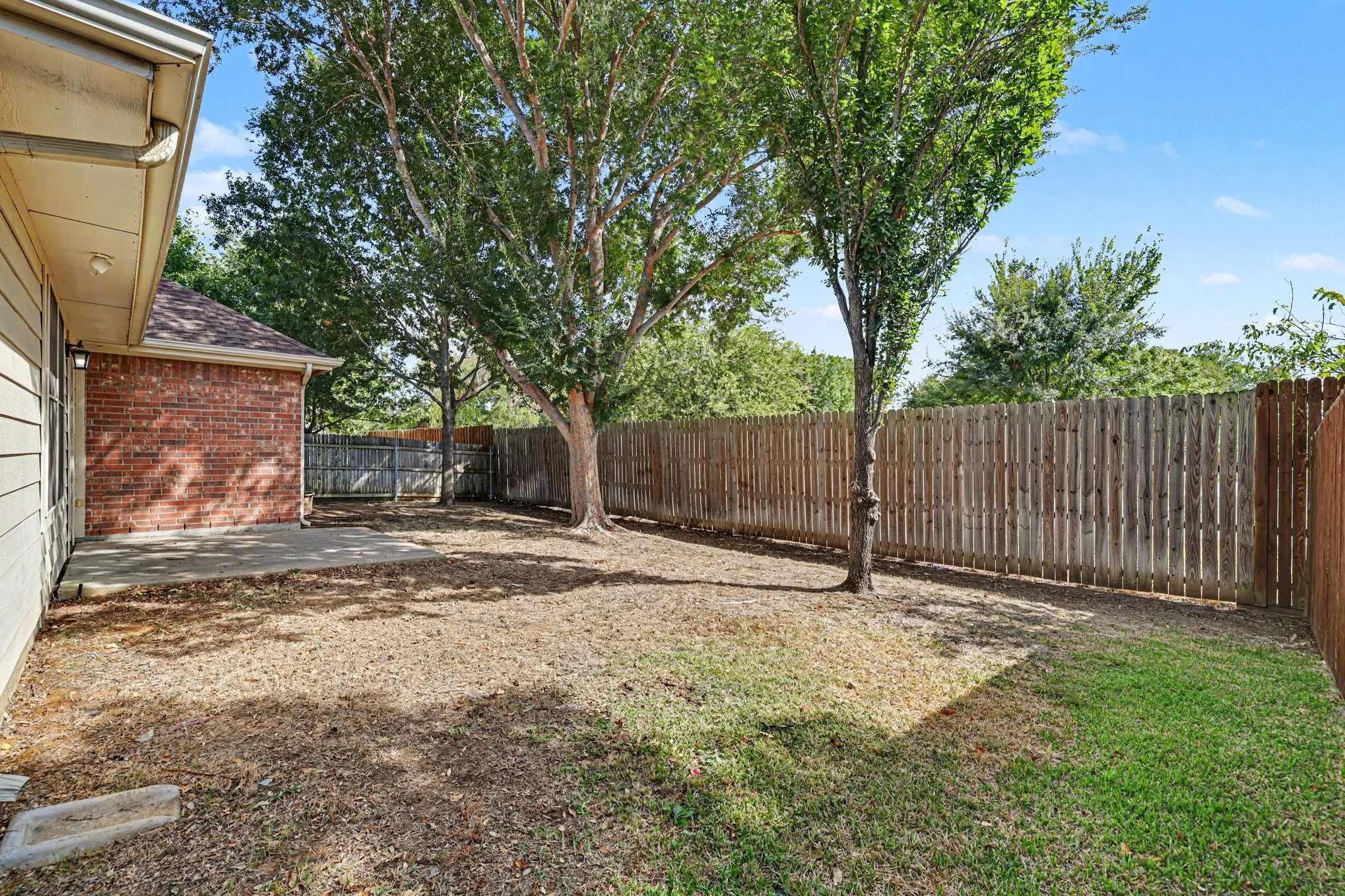 Private backyard featuring a concrete patio, wood privacy fencing, and established trees