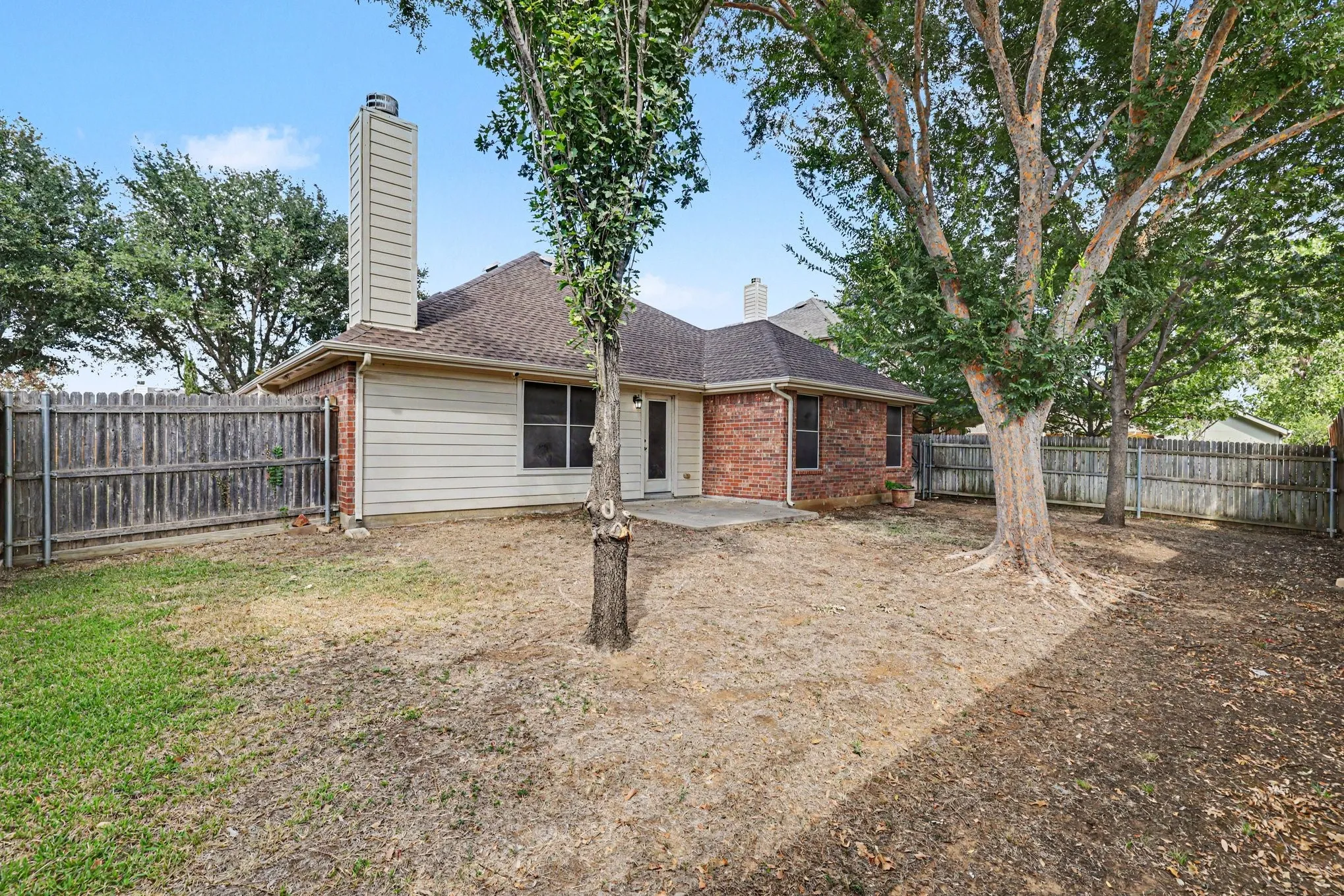 Expansive backyard featuring mature trees, a privacy fence, and a concrete patio