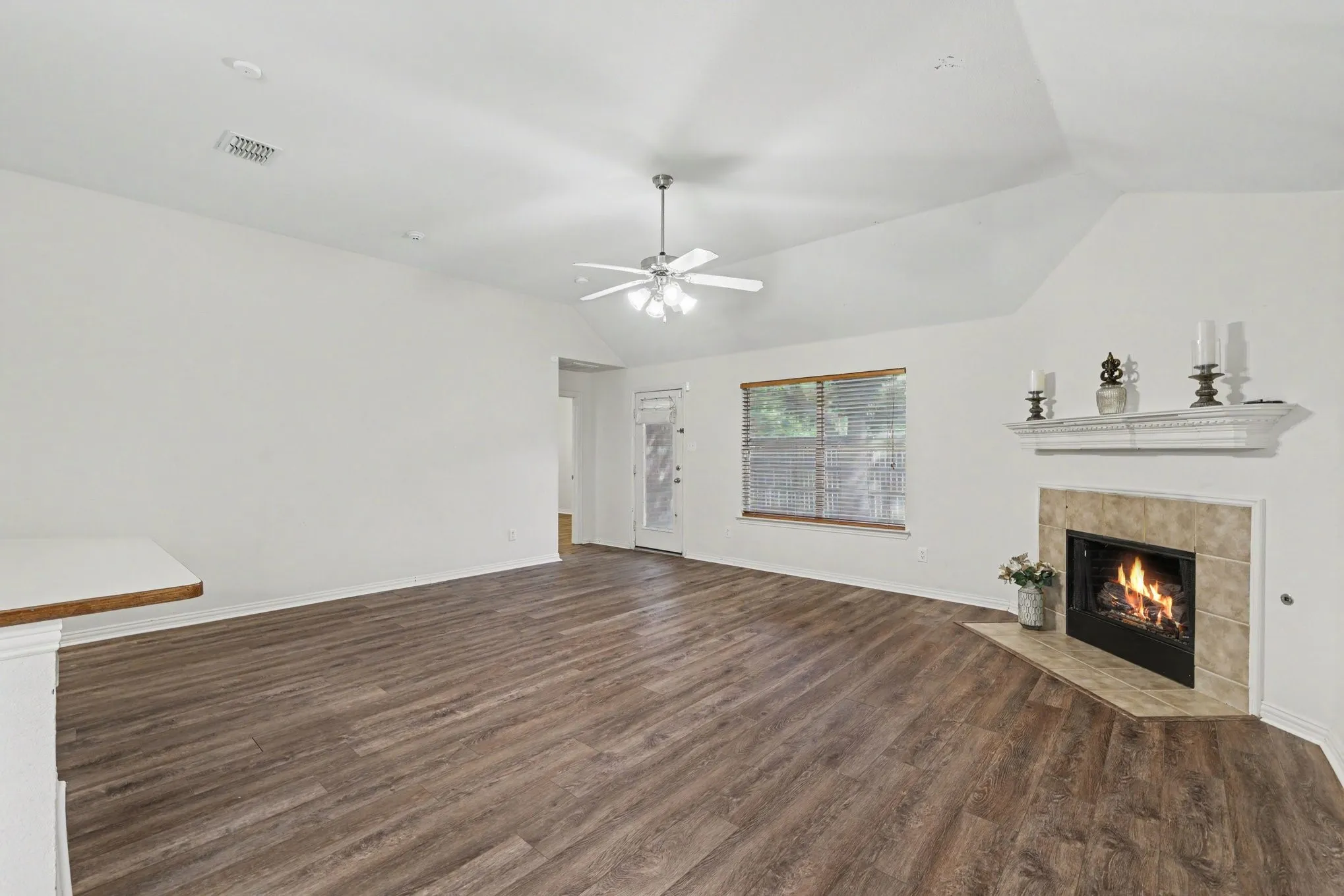 Vaulted ceiling with a ceiling fan, wood-finish flooring, recessed lighting, and a corner fireplace with a tile surround and mantel
