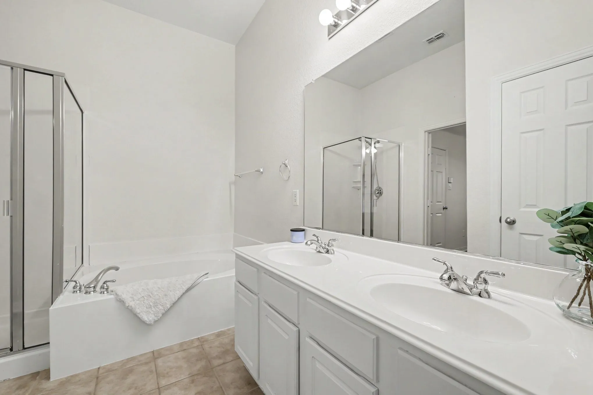 Dual vanity with integrated sinks, chrome fixtures, built-in bathtub, and an enclosed shower with a clear glass door