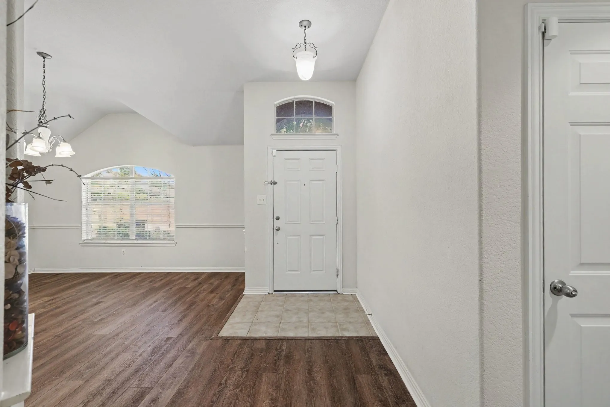 Vaulted ceilings, wood-finish flooring, arched window, tile flooring at entry, and an overhead light fixture