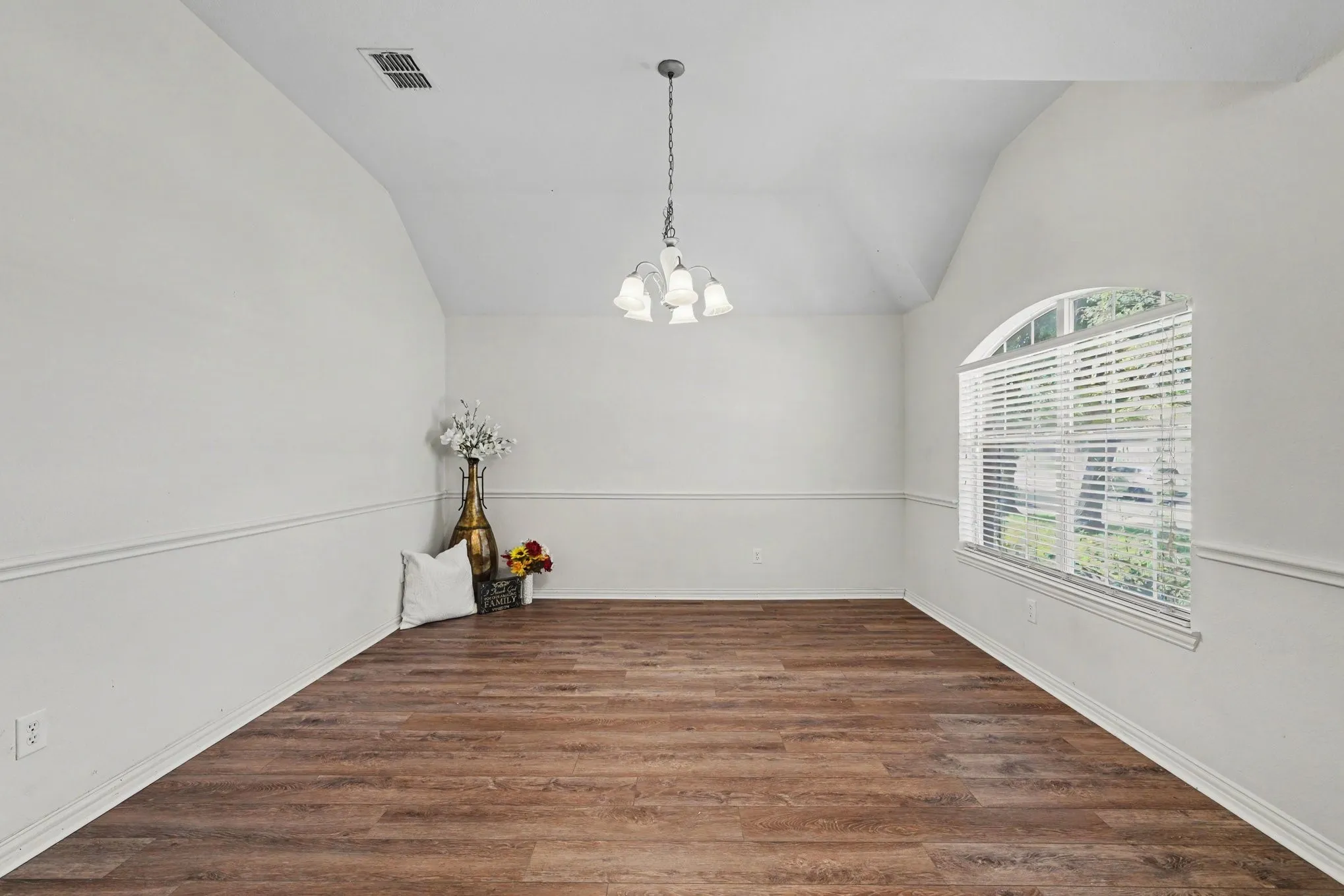 Vaulted ceiling, wood-finish flooring, decorative chair rail molding, arched window, and a hanging chandelier