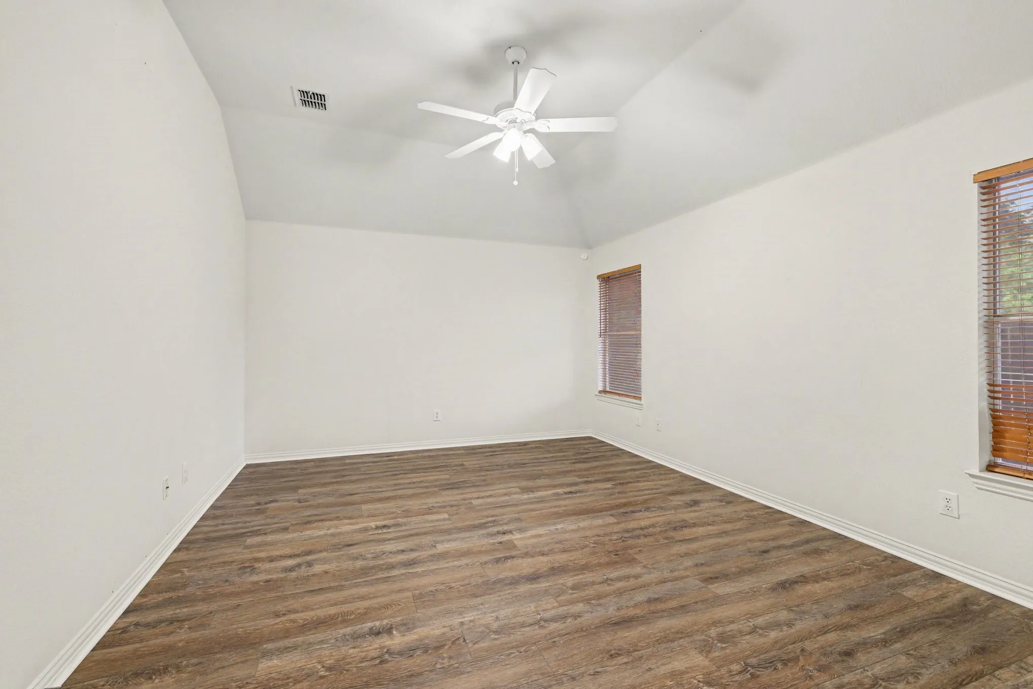 Vaulted ceiling, wood-finish flooring, ceiling fan, and two windows with wood blinds