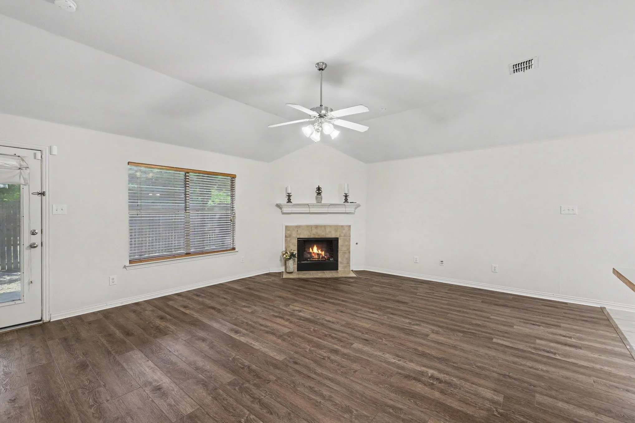 Vaulted ceiling with a ceiling fan, fireplace with a mantel, tile surround, wood-finish flooring, and a glass-paneled door
