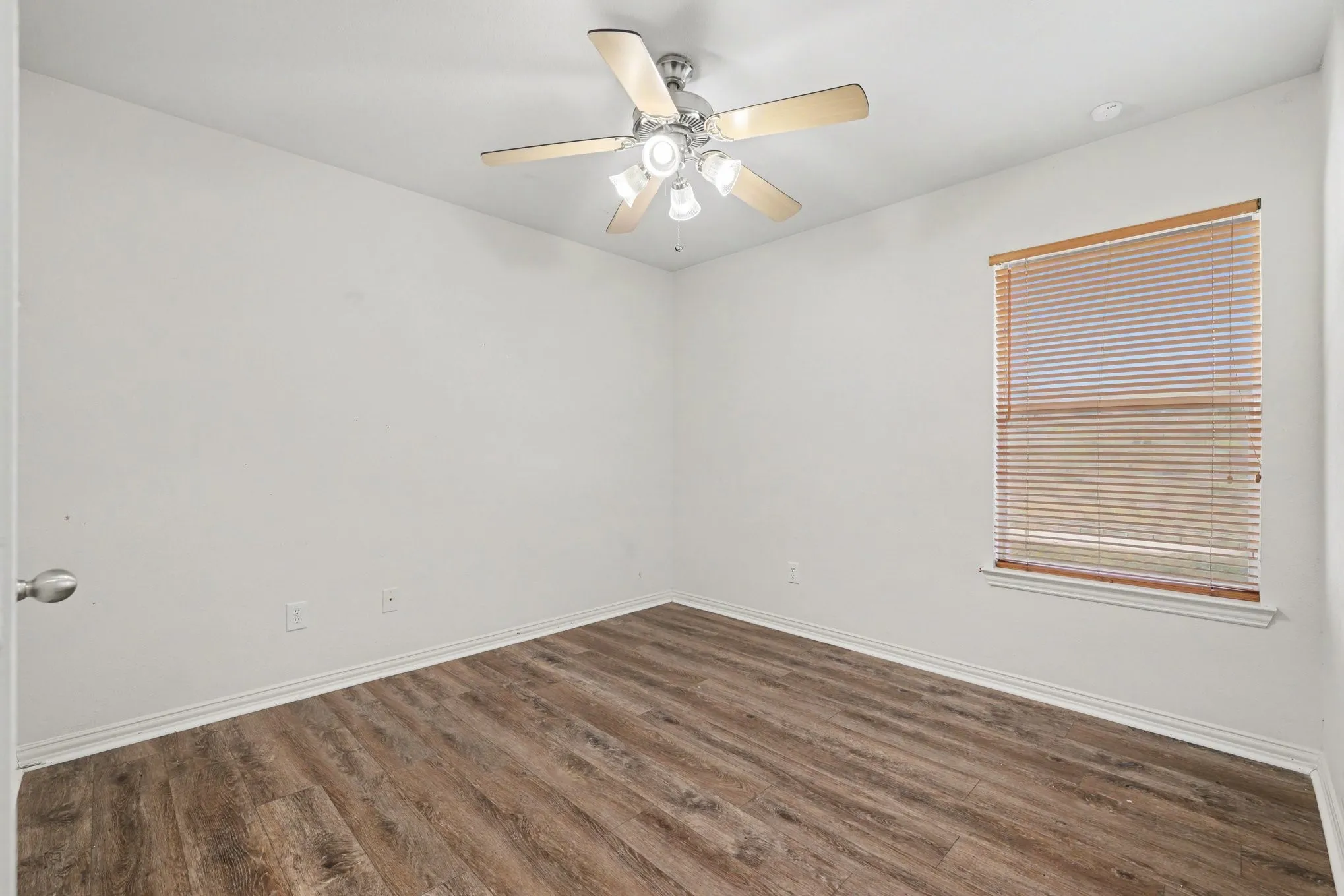 Wood-finish flooring, ceiling fan with integrated lighting, window with blinds, and white trim