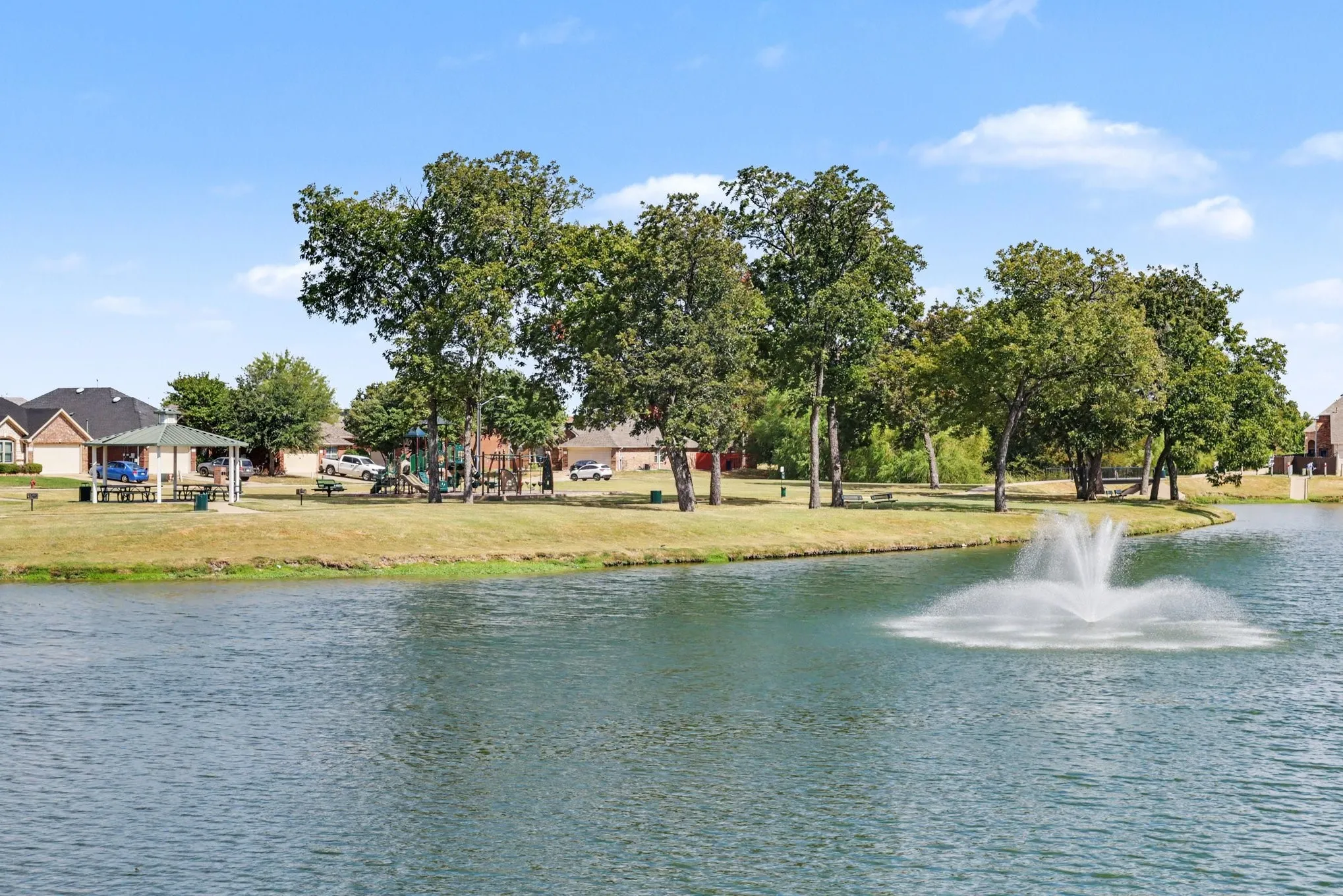 Water feature with fountain, surrounding green space, mature trees, and nearby sheltered picnic area