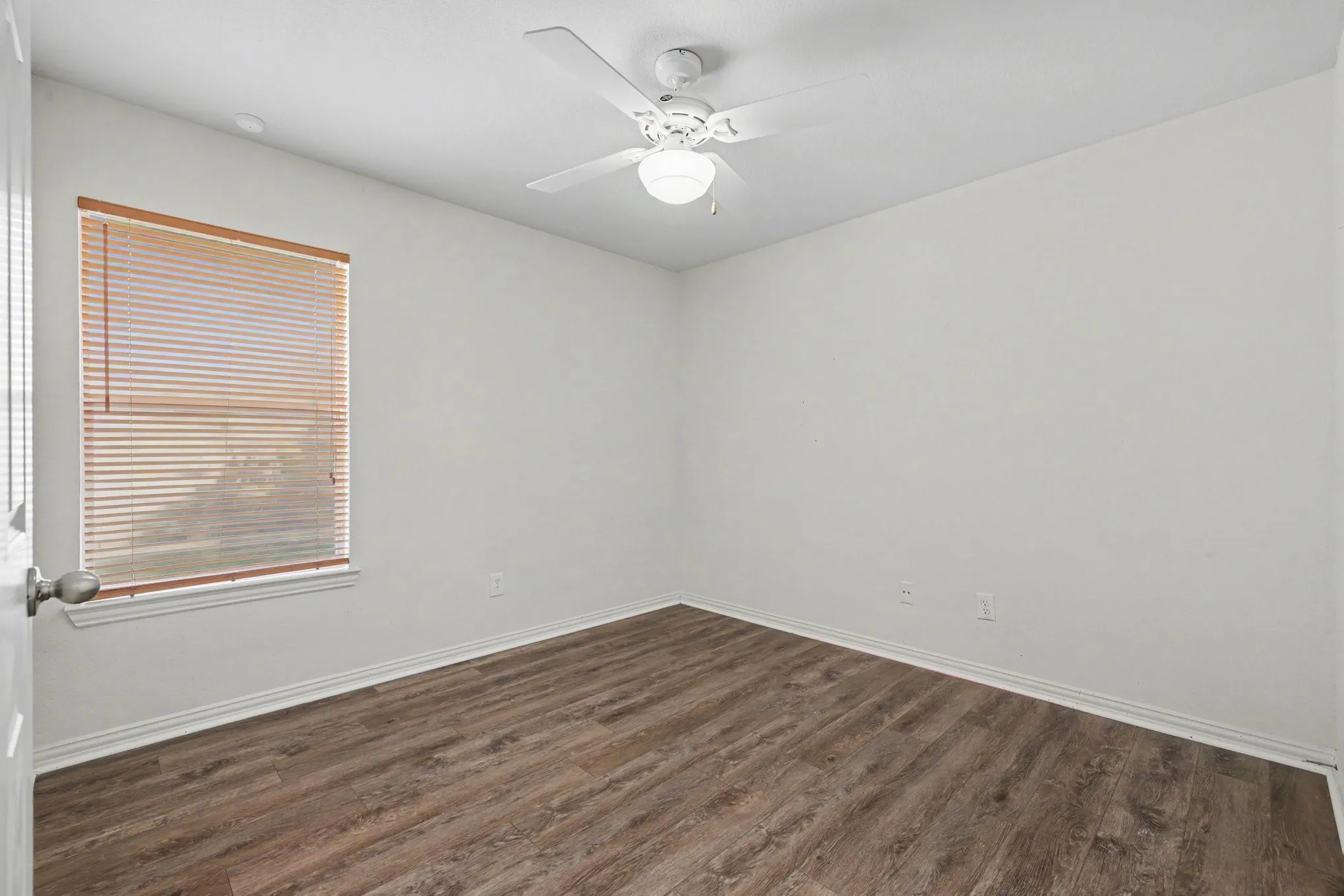 Wood-finish flooring with white baseboards, a window with blinds, and a ceiling fan with integrated lighting