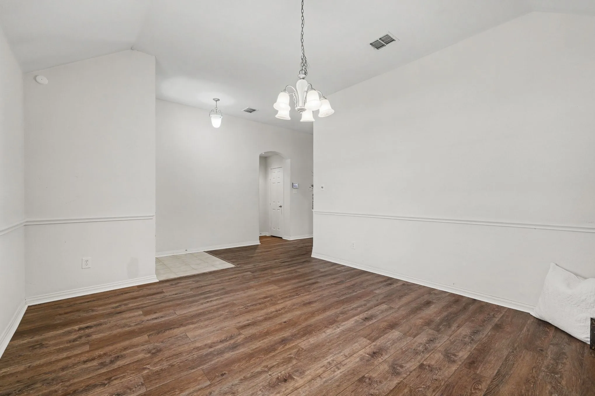 Vaulted ceiling with a chandelier, wood-finish flooring, half-wall molding, and arched doorway