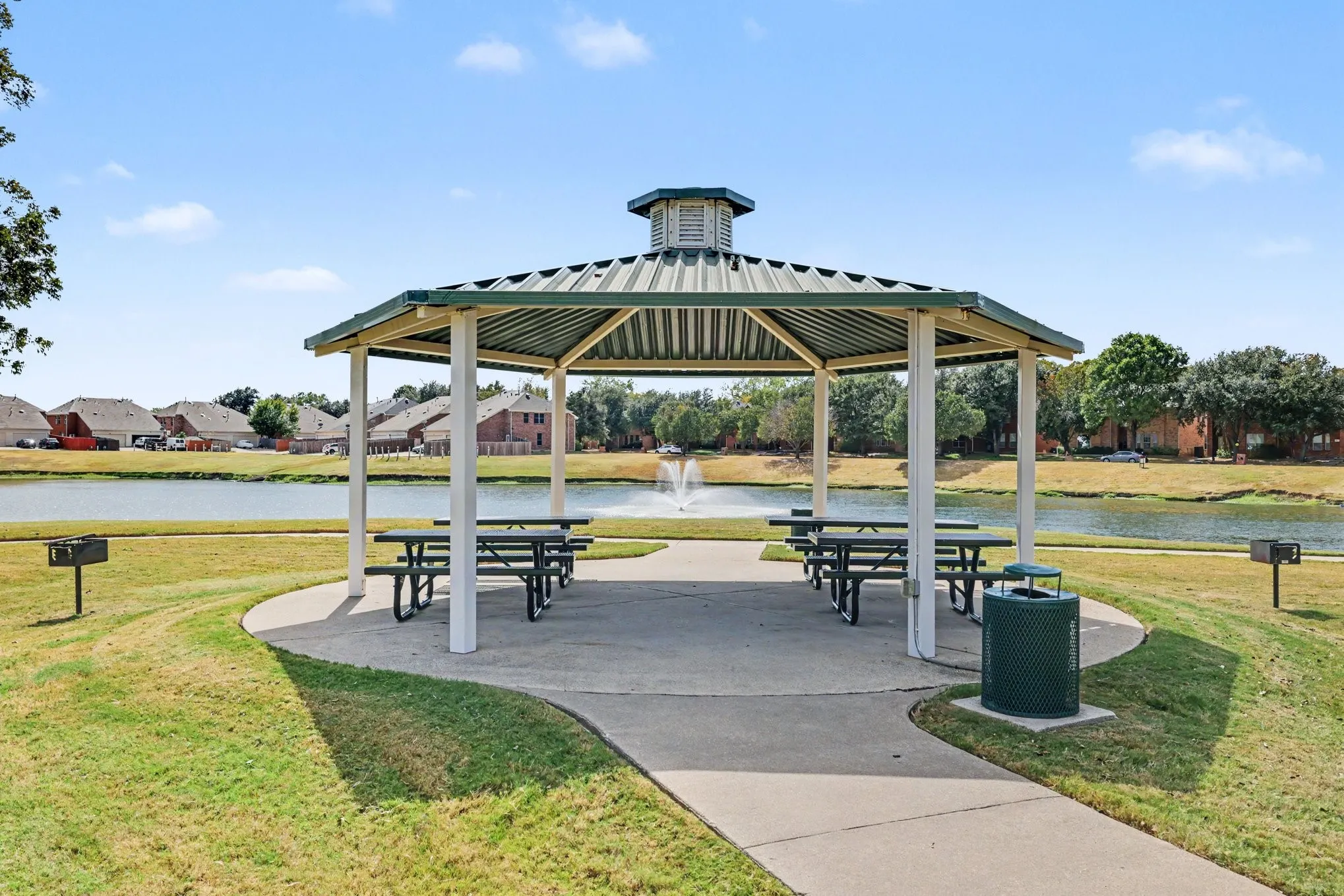 Metal-roofed gazebo with four picnic tables on a curved concrete pad