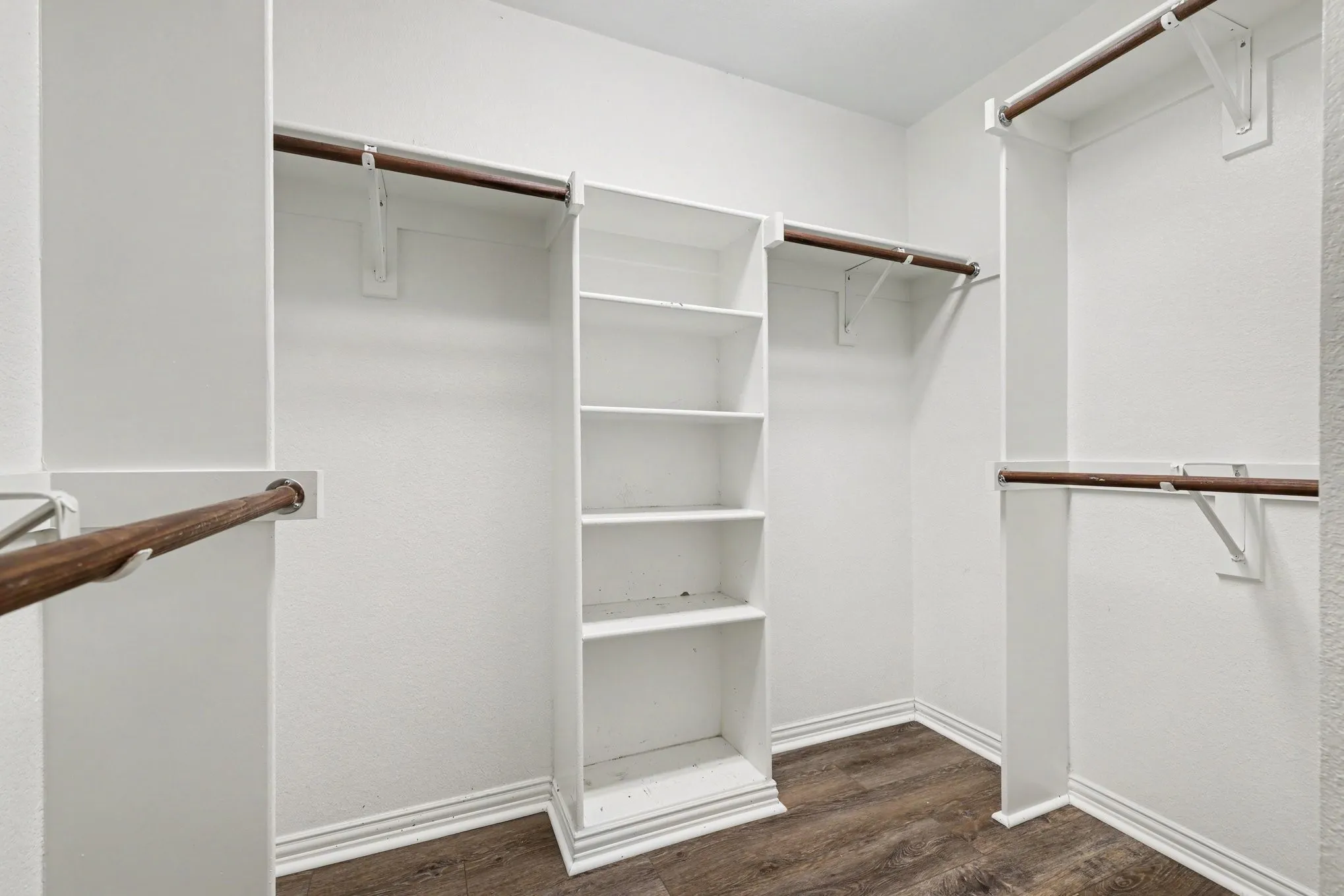Walk-in closet featuring white built-in shelving, multiple hanging rods, and wood-finish flooring