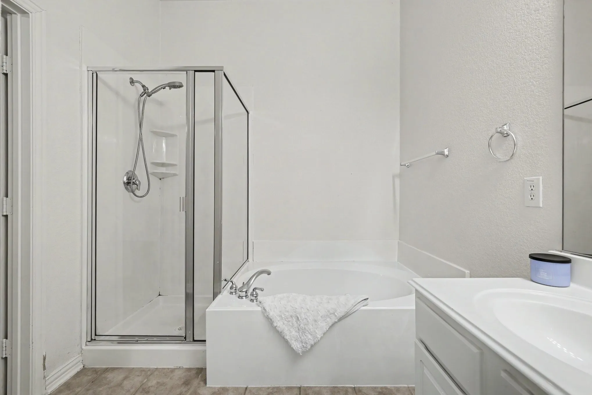 Walk-in shower with glass enclosure, separate soaking tub, single vanity with integrated sink, and wood-finish flooring