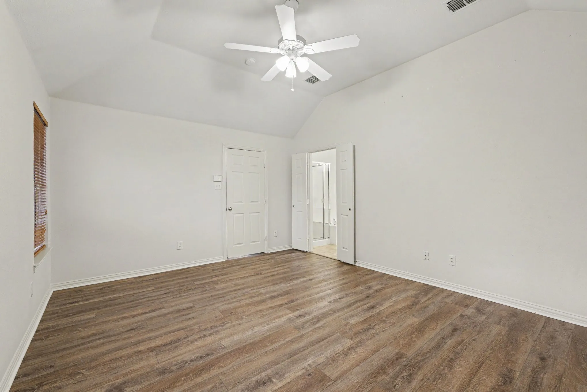 Vaulted ceiling with a ceiling fan, wood-finish flooring, and white interior doors