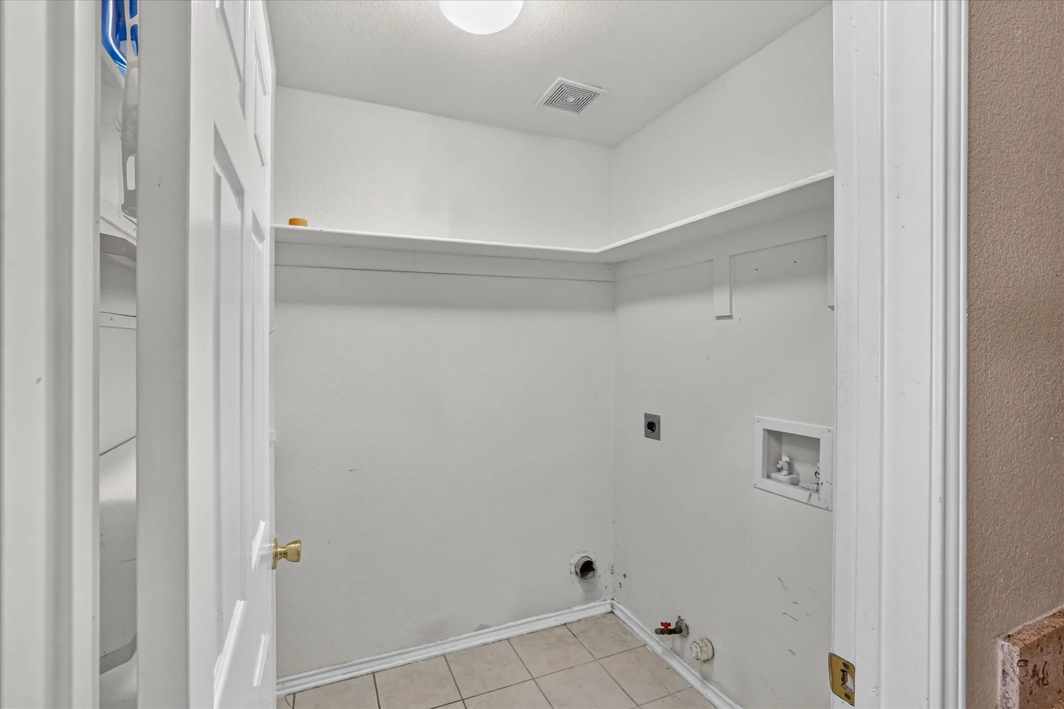 Utility space featuring a built-in shelf, tiled flooring, and wall-mounted plumbing connections