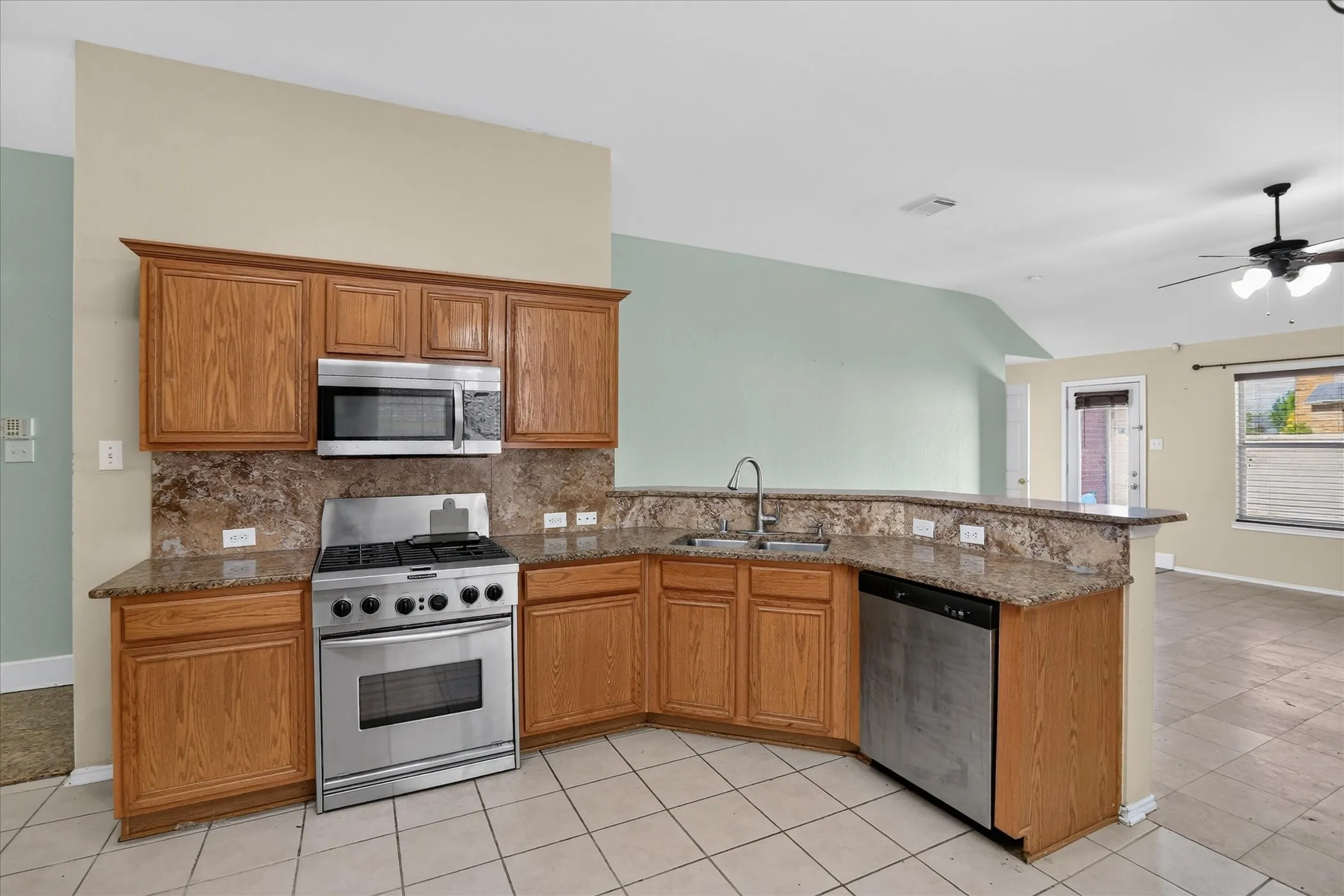Kitchen featuring wood cabinetry, stainless steel appliances, tile flooring, stone countertops, and a breakfast bar