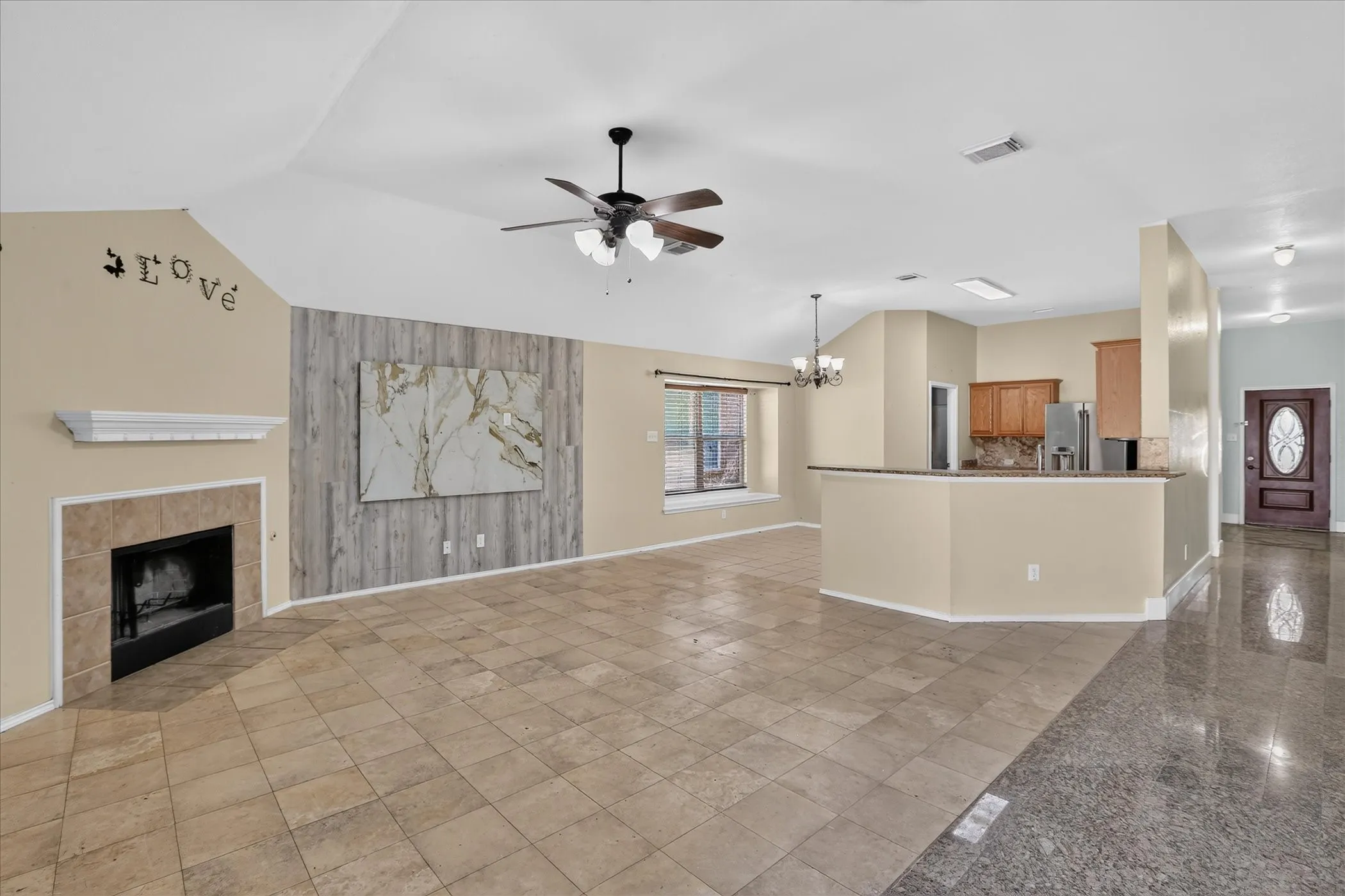 Vaulted ceiling, ceiling fan, fireplace with mantel, tiled flooring, and wood-finish accent wall