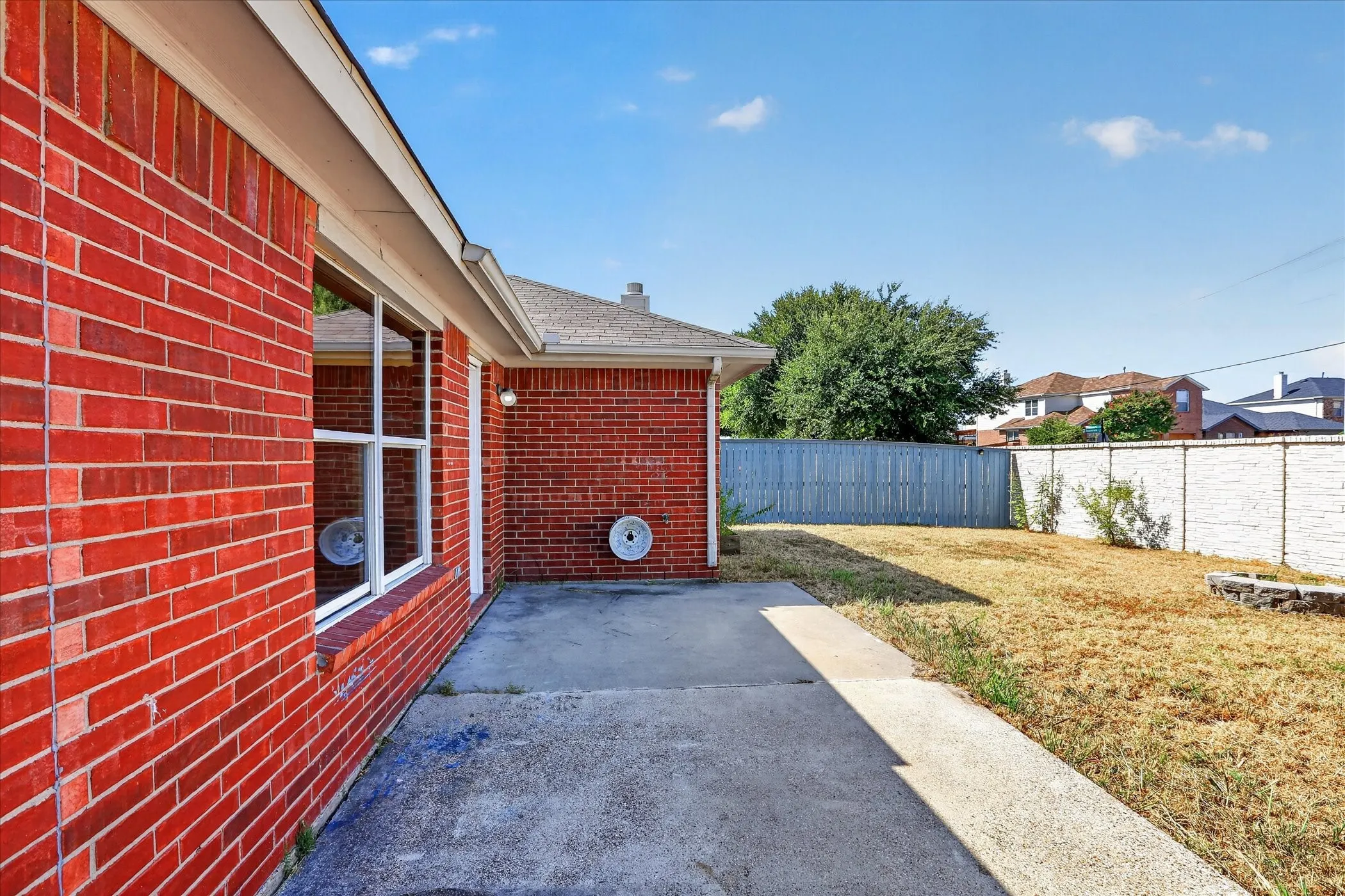 Red brick exterior with white window trim, concrete patio, and a fenced backyard